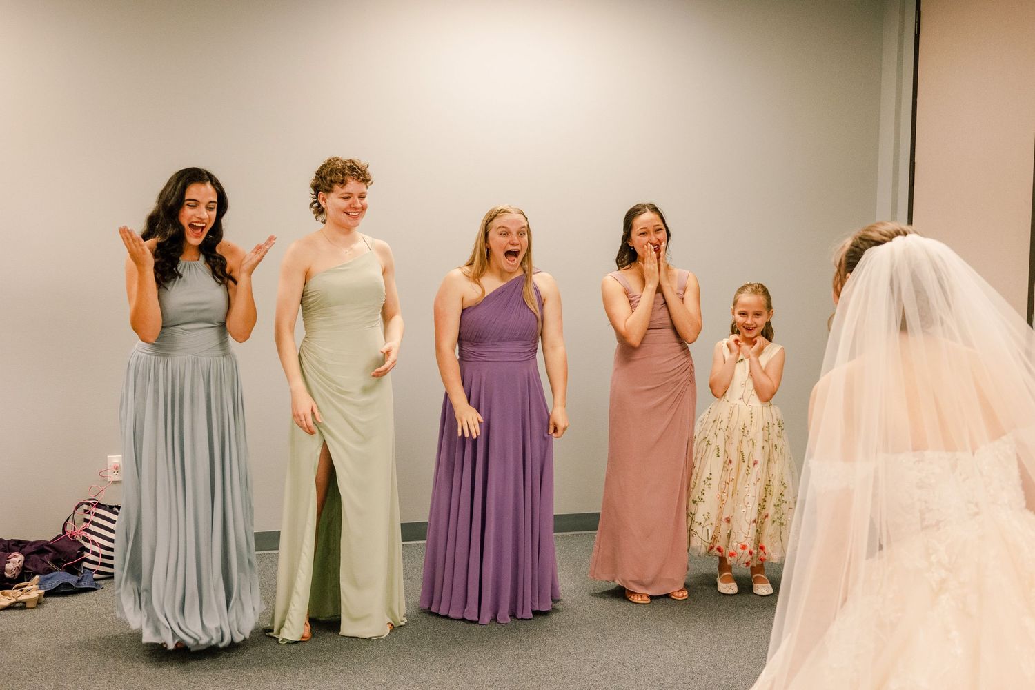 Bridesmaids in pastel colored dresses help prepare a bride in a white gown during wedding preparations.