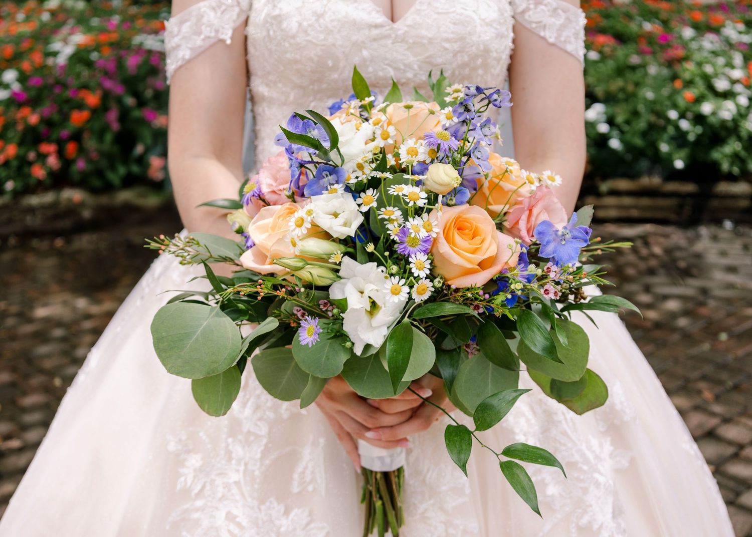 A vibrant wedding bouquet featuring peach roses, purple flowers, and eucalyptus leaves.