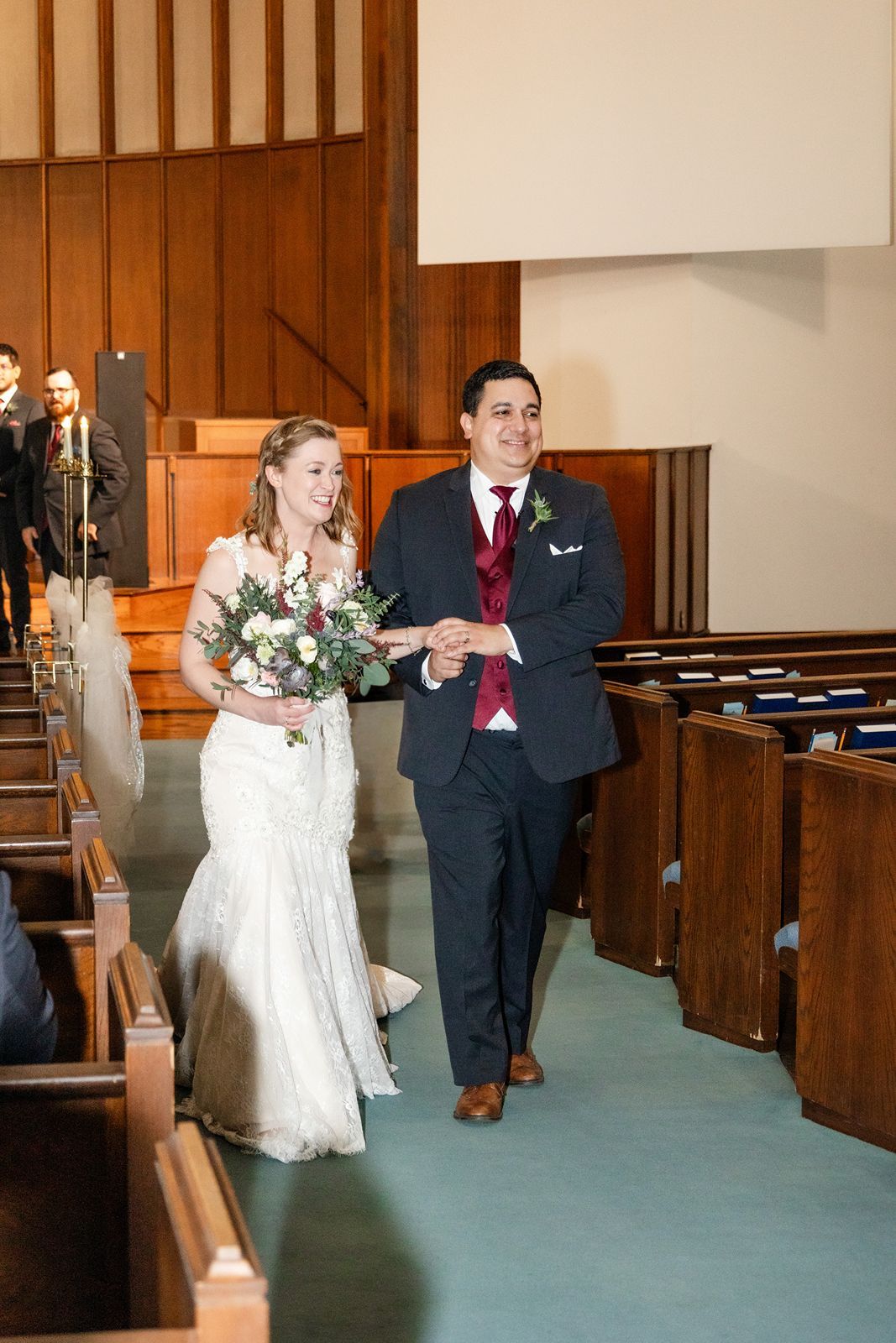 Bride and groom walk down church aisle smiling after wedding ceremony.
