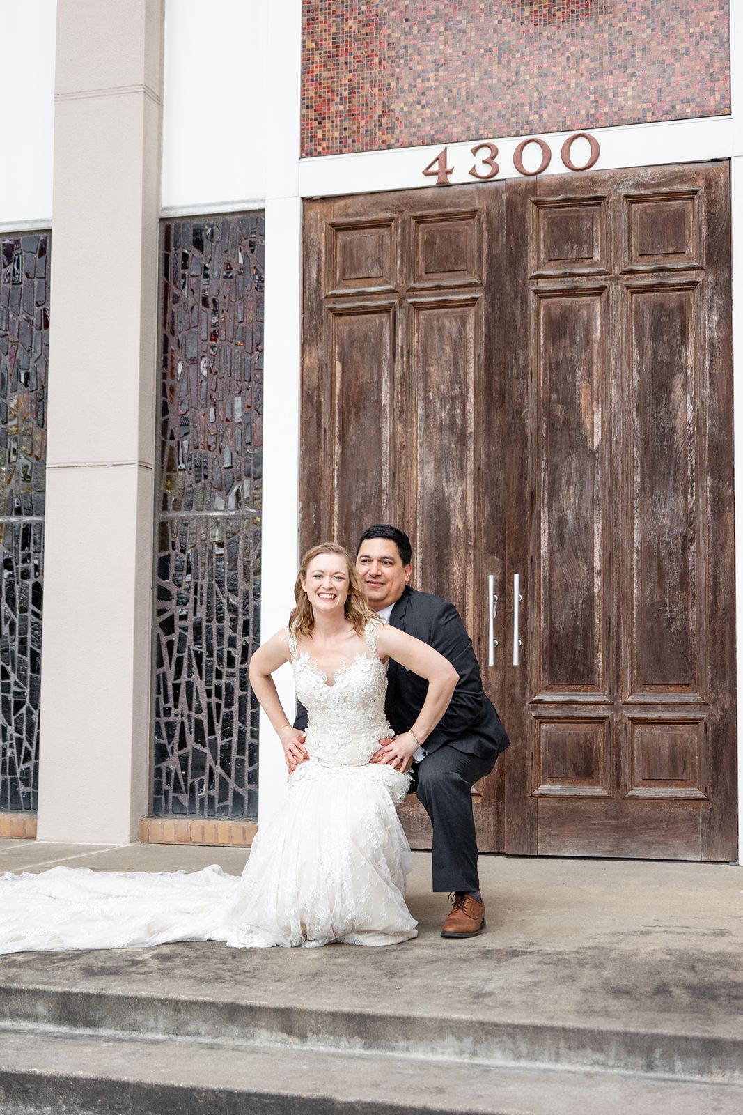 Smiling bride and groom posing on steps before large wooden doors at 4300 wedding venue.
