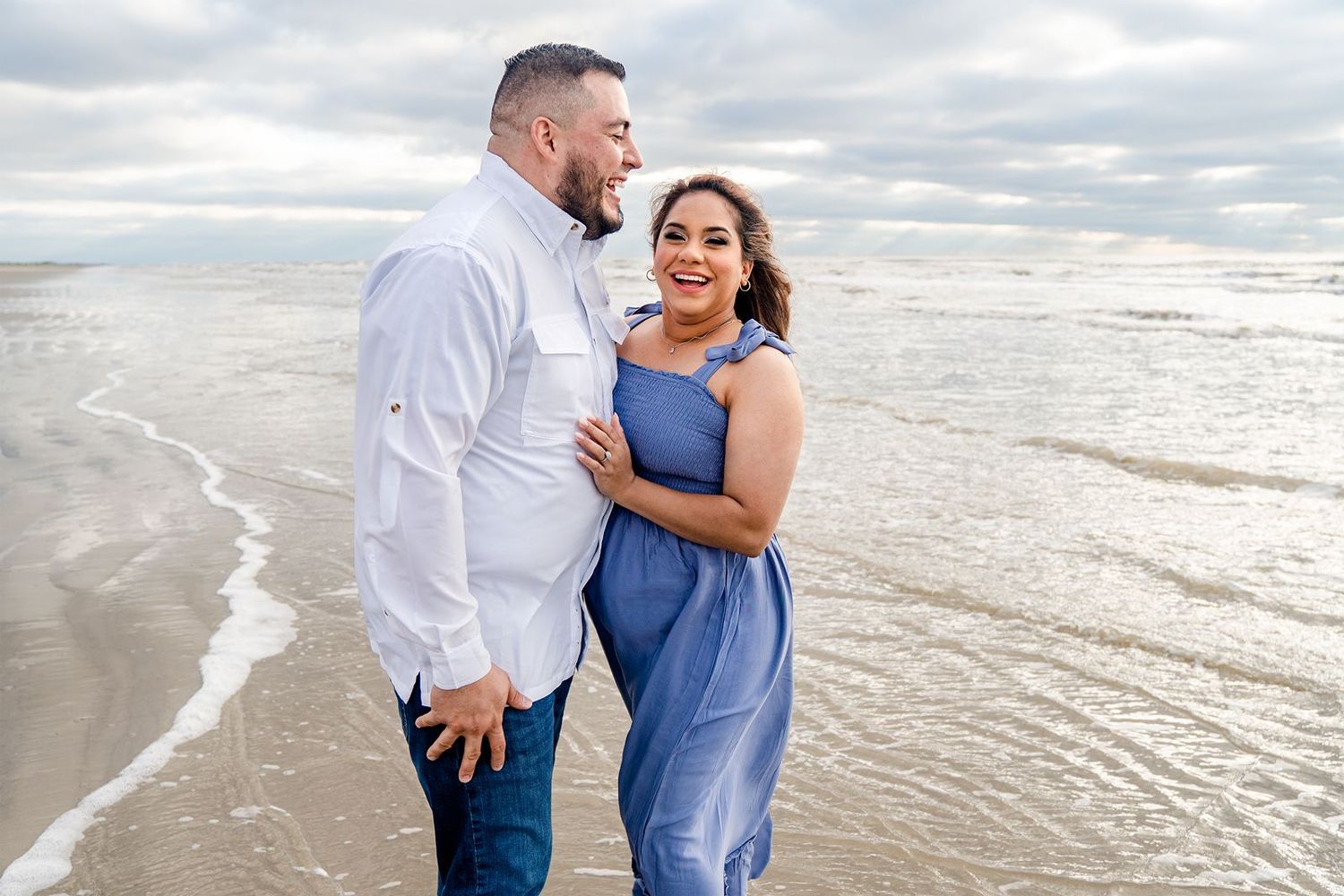 A couple shares a romantic moment while walking along the beach at sunset with waves rolling onto shore.