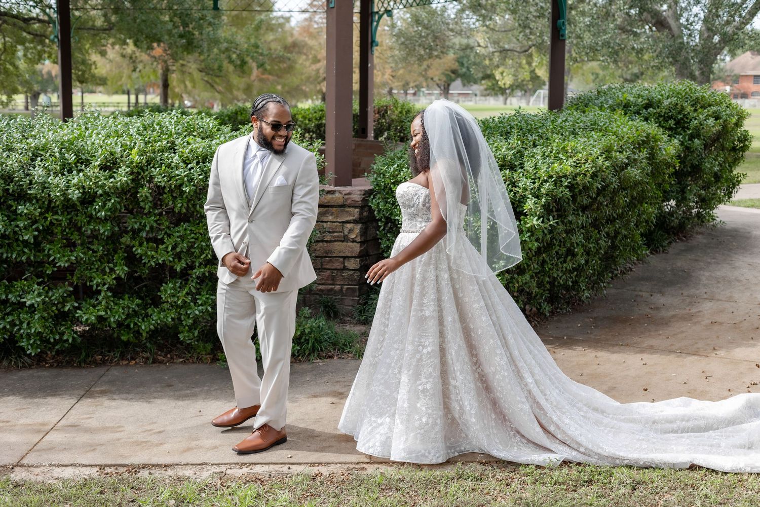Wedding couple poses together in a garden setting wearing white formal attire and a flowing bridal gown.