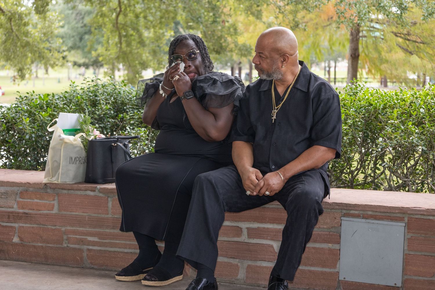 Wedding guests in dark formal attire relax on brick ledges during an outdoor reception.