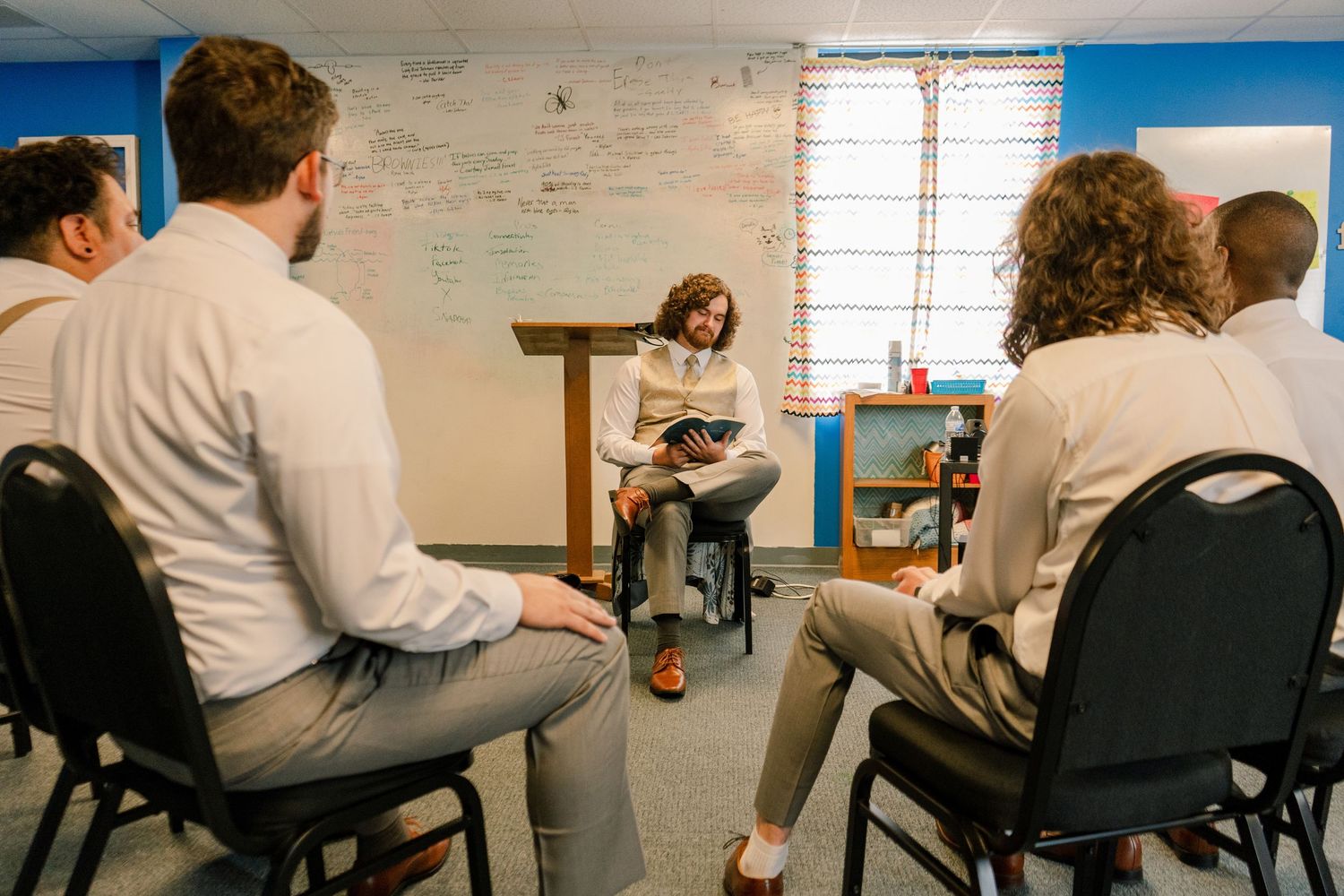 People seated in chairs in a casual meeting room setting with blue walls.