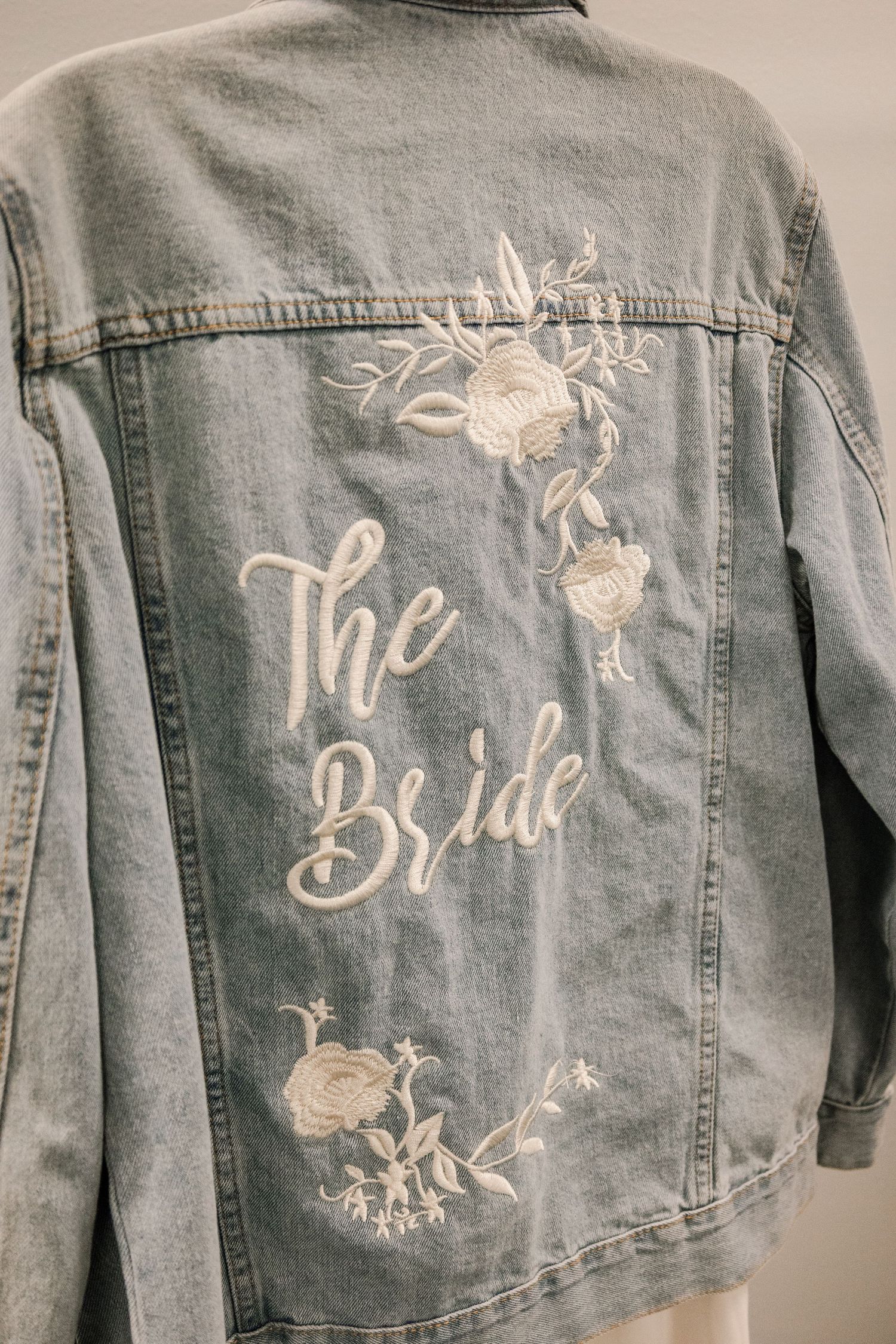 Customized denim jackets with white embroidered bridal party titles and floral designs.