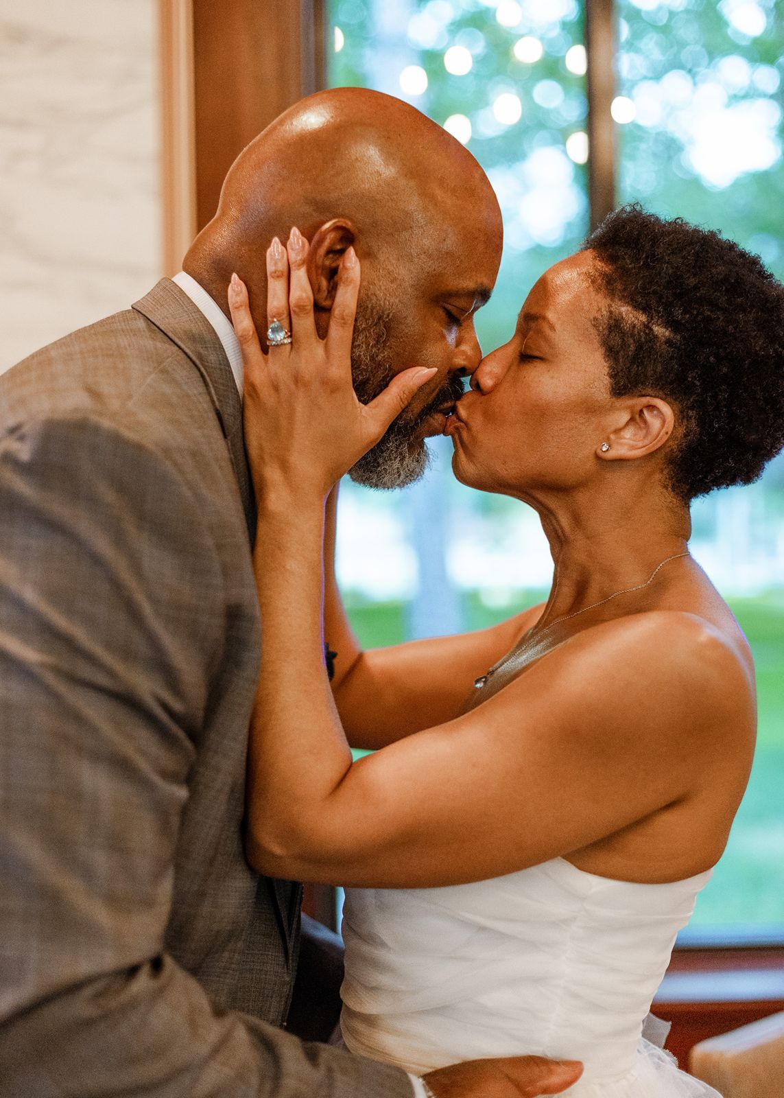 A newlywed couple shares a romantic kiss, with the bride tenderly holding the grooms face during their wedding ceremony.