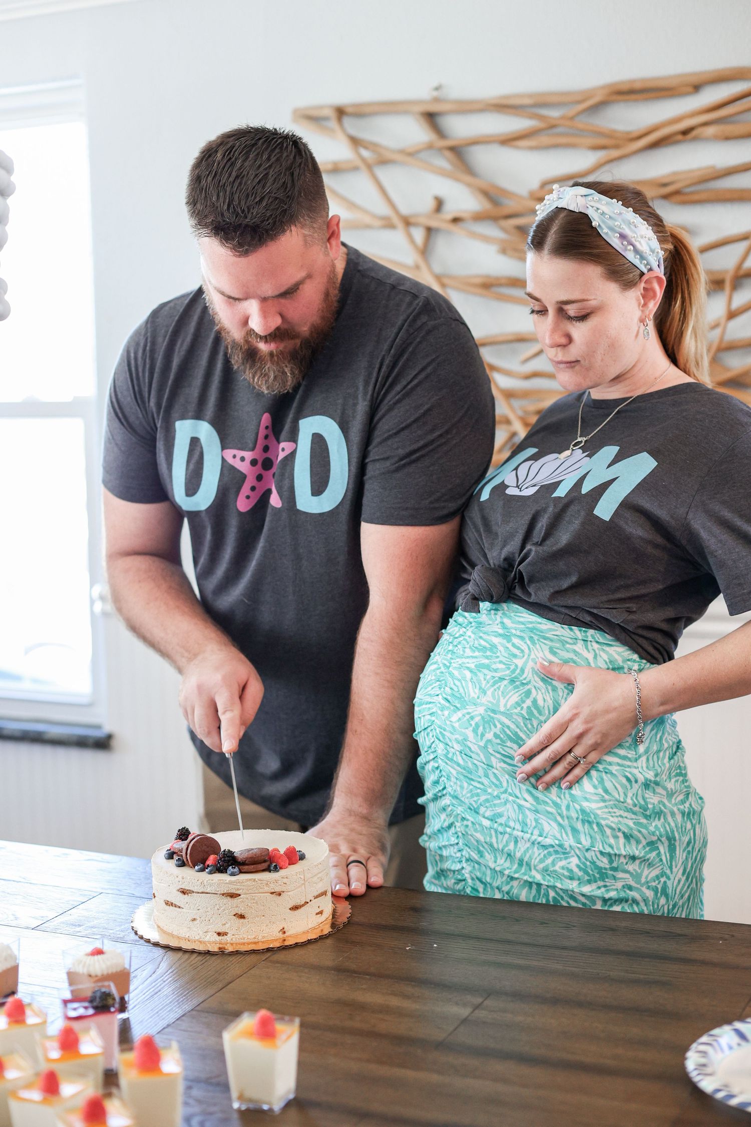 Two people in dark shirts decorate a white cake with fresh berries on a wooden table.