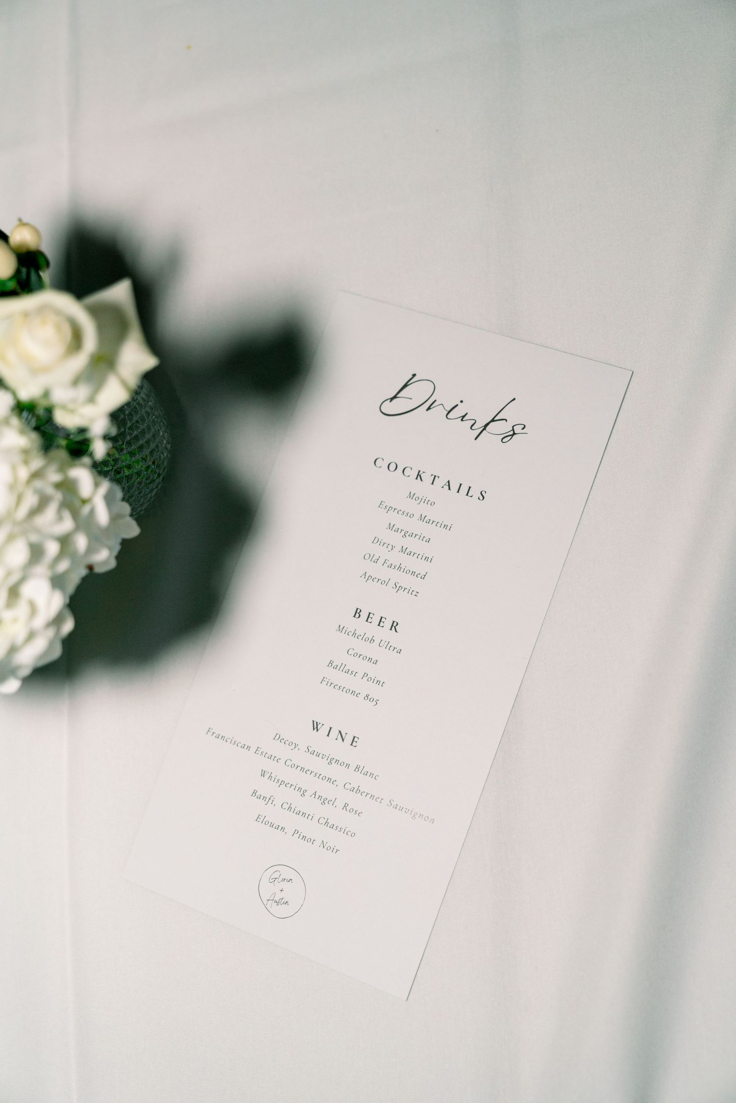 Elegant wedding menu card featuring drinks list with white roses in soft focus background.