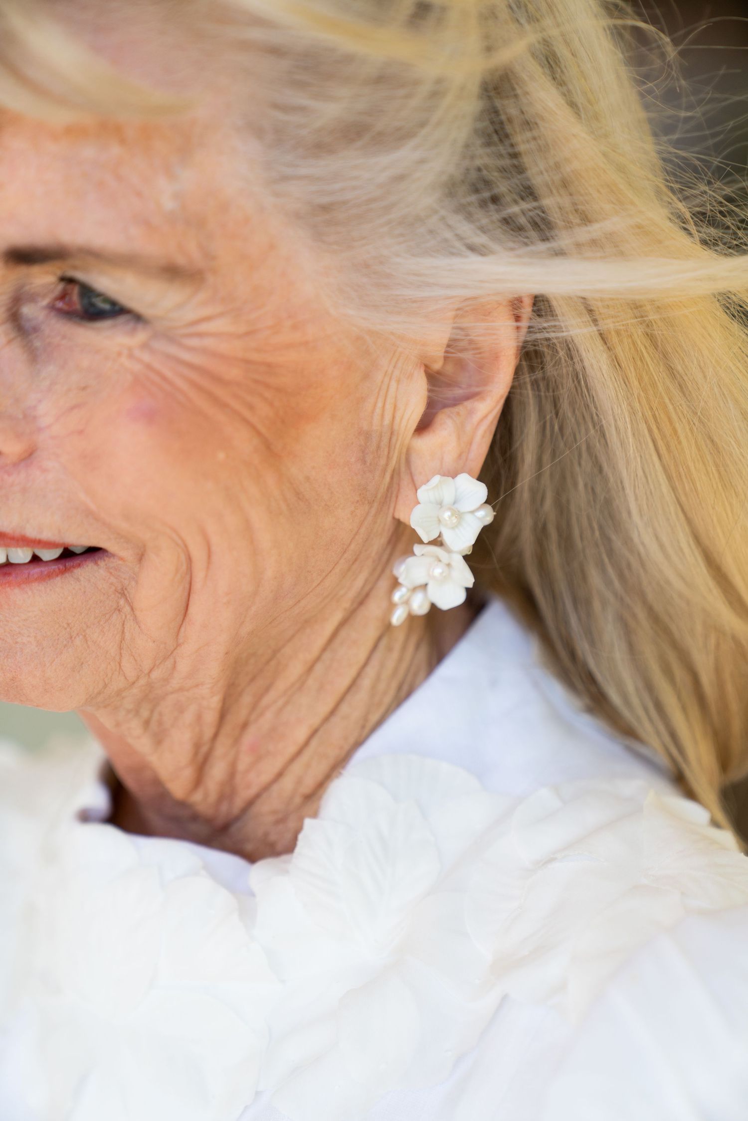 Delicate white flower earrings worn with flowing blonde hair in a close-up side profile shot.