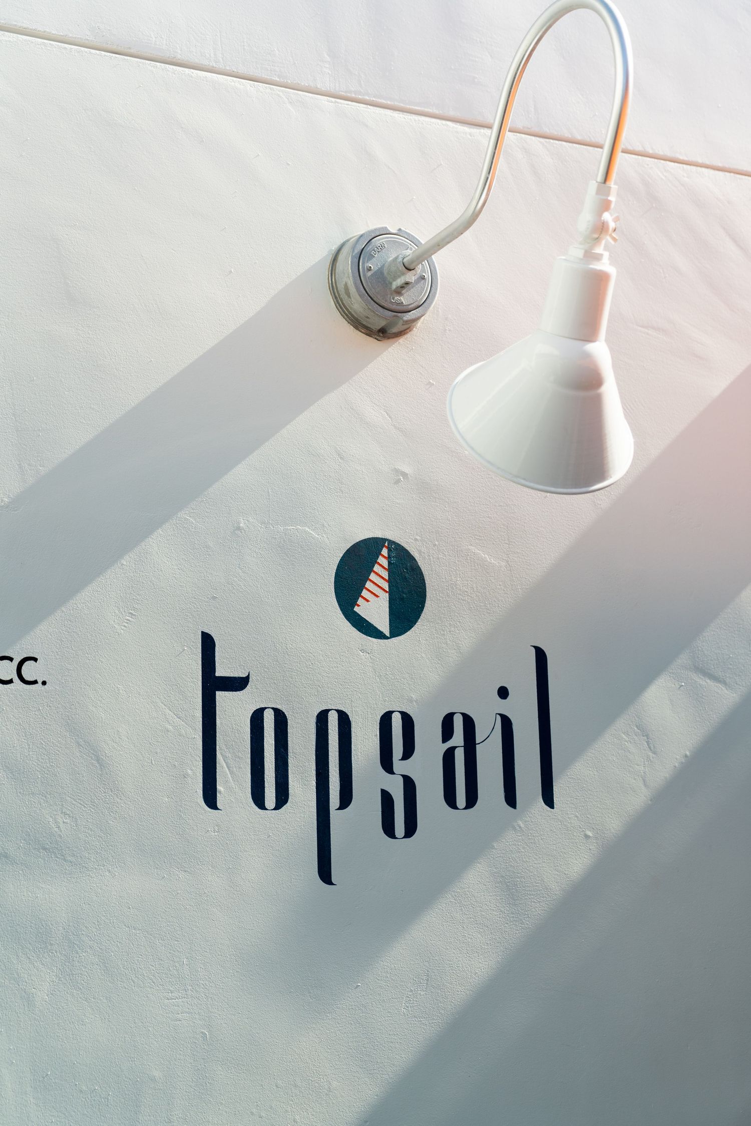 A white wall-mounted lamp hangs above a blue Topsail logo and icon design.