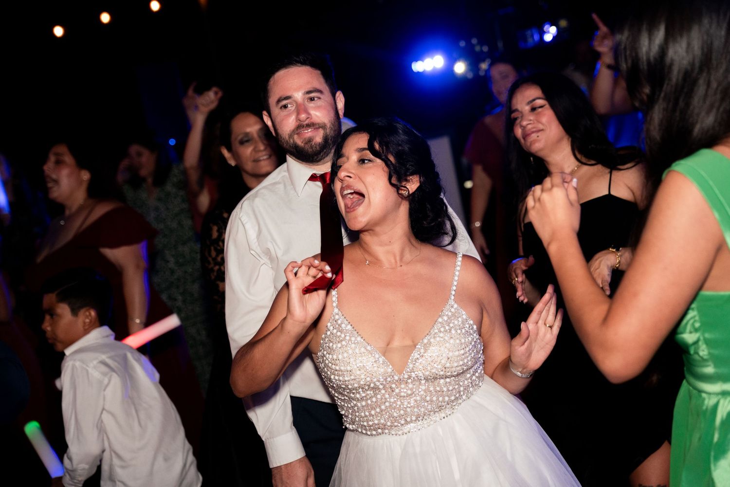 Wedding celebration on dance floor with festive lighting and energetic dancing.