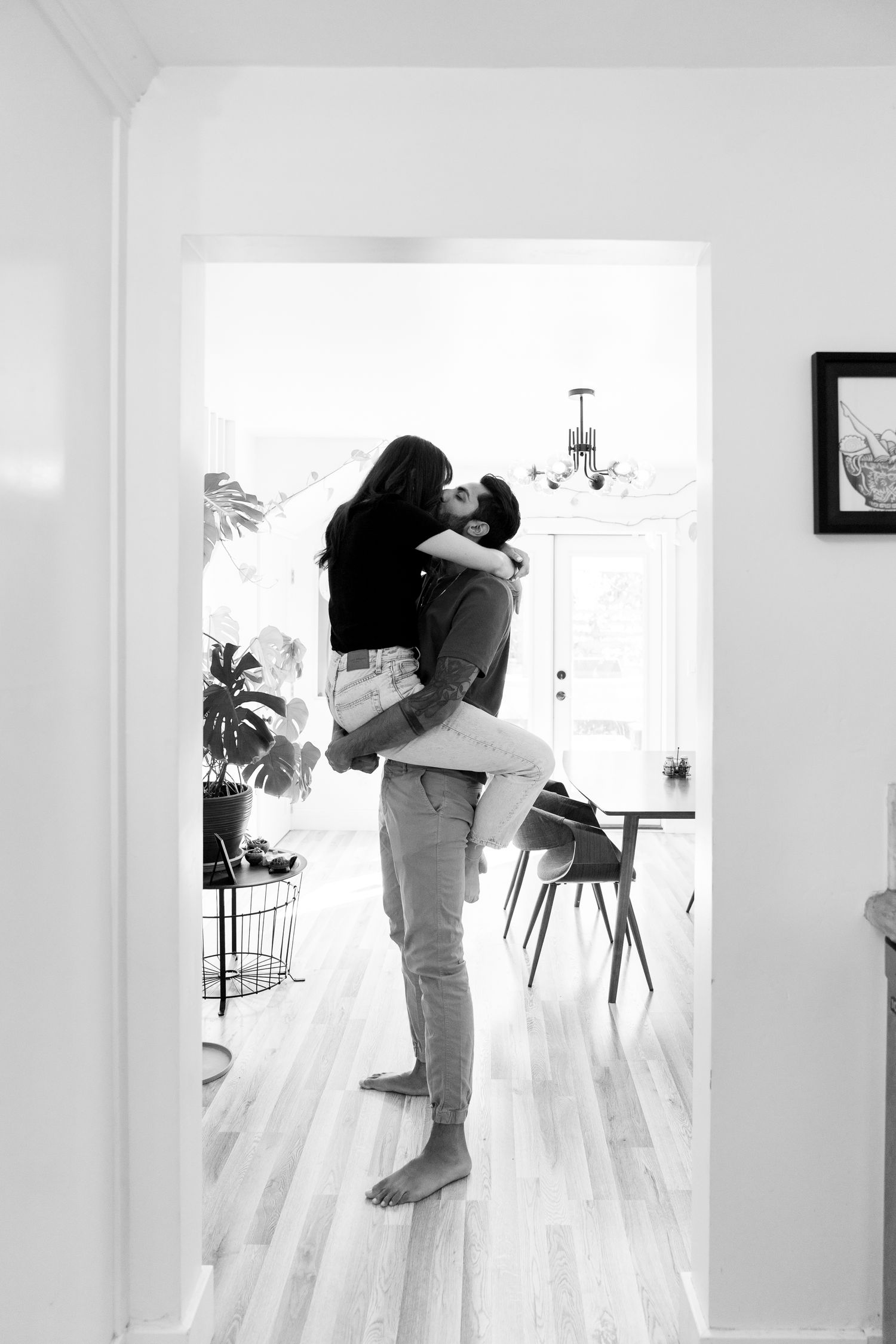 A tender black and white moment of two people embracing in a bright minimalist room with hardwood floors.