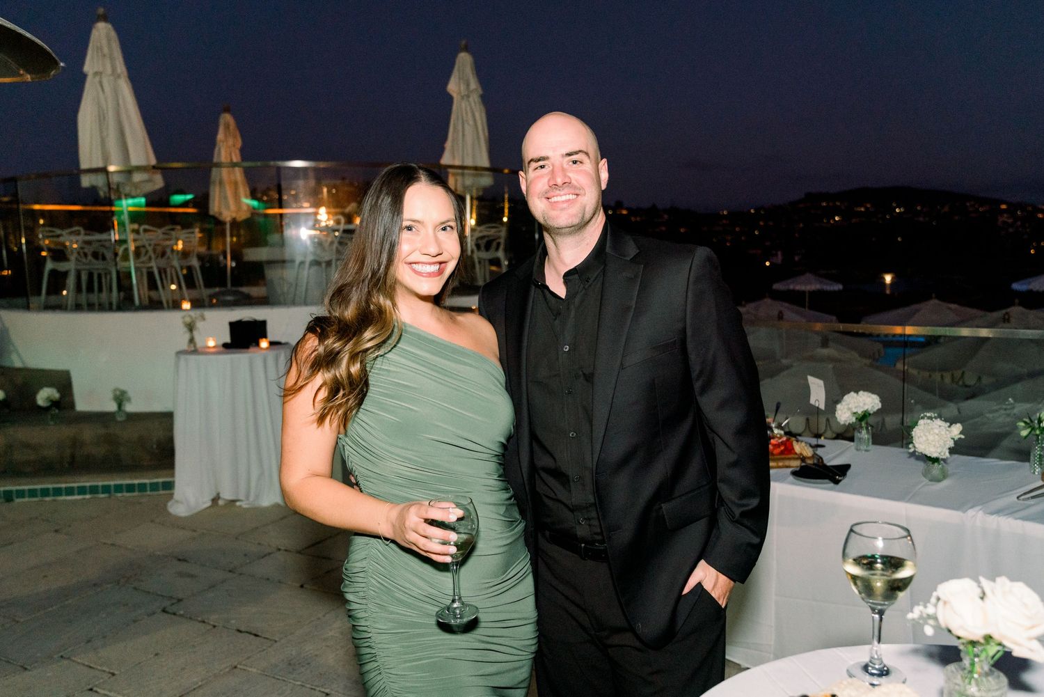 Elegant evening event on a rooftop terrace with city lights in background.