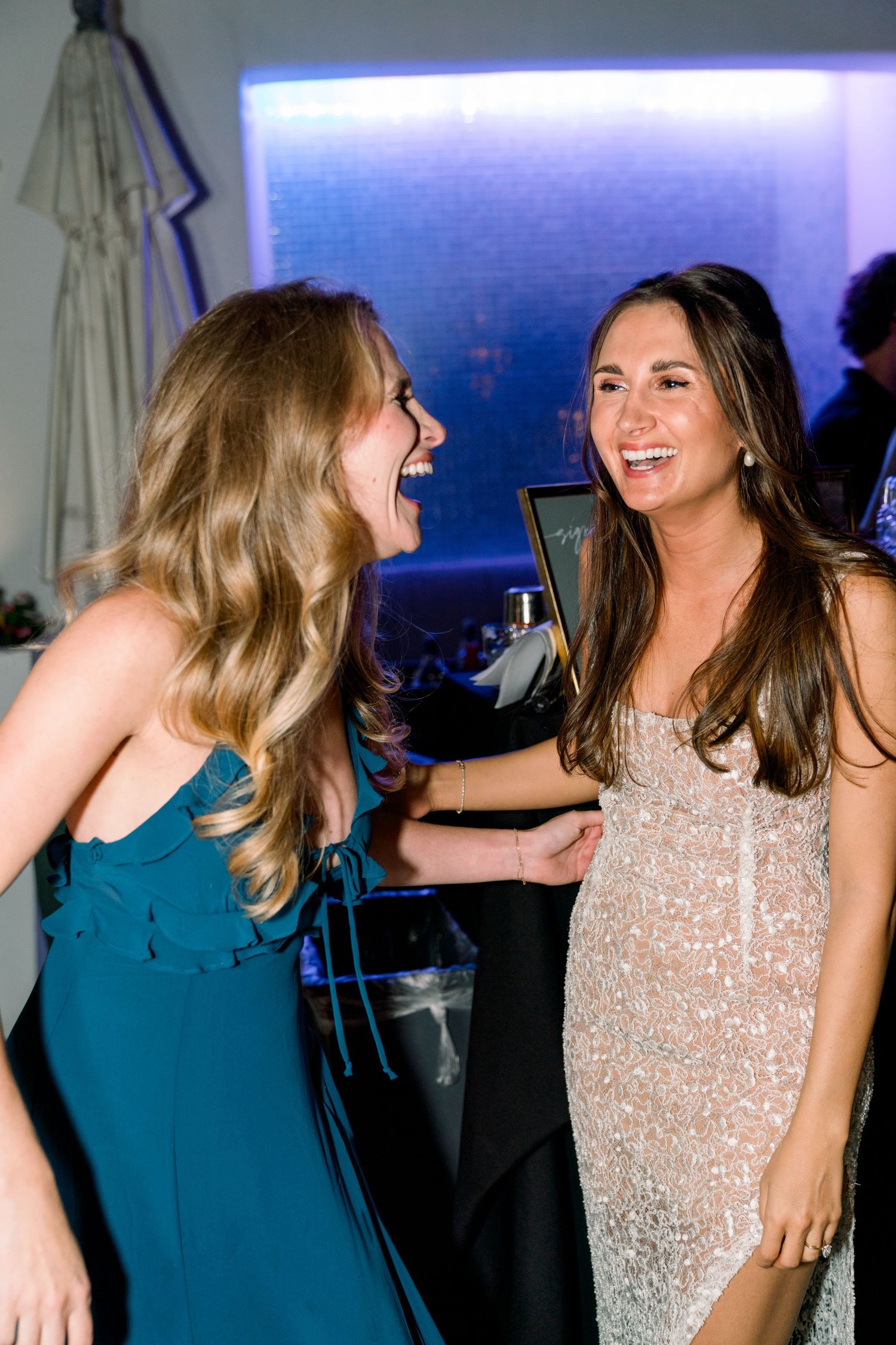 Two women in formal dresses share a joyful moment at an evening celebration.