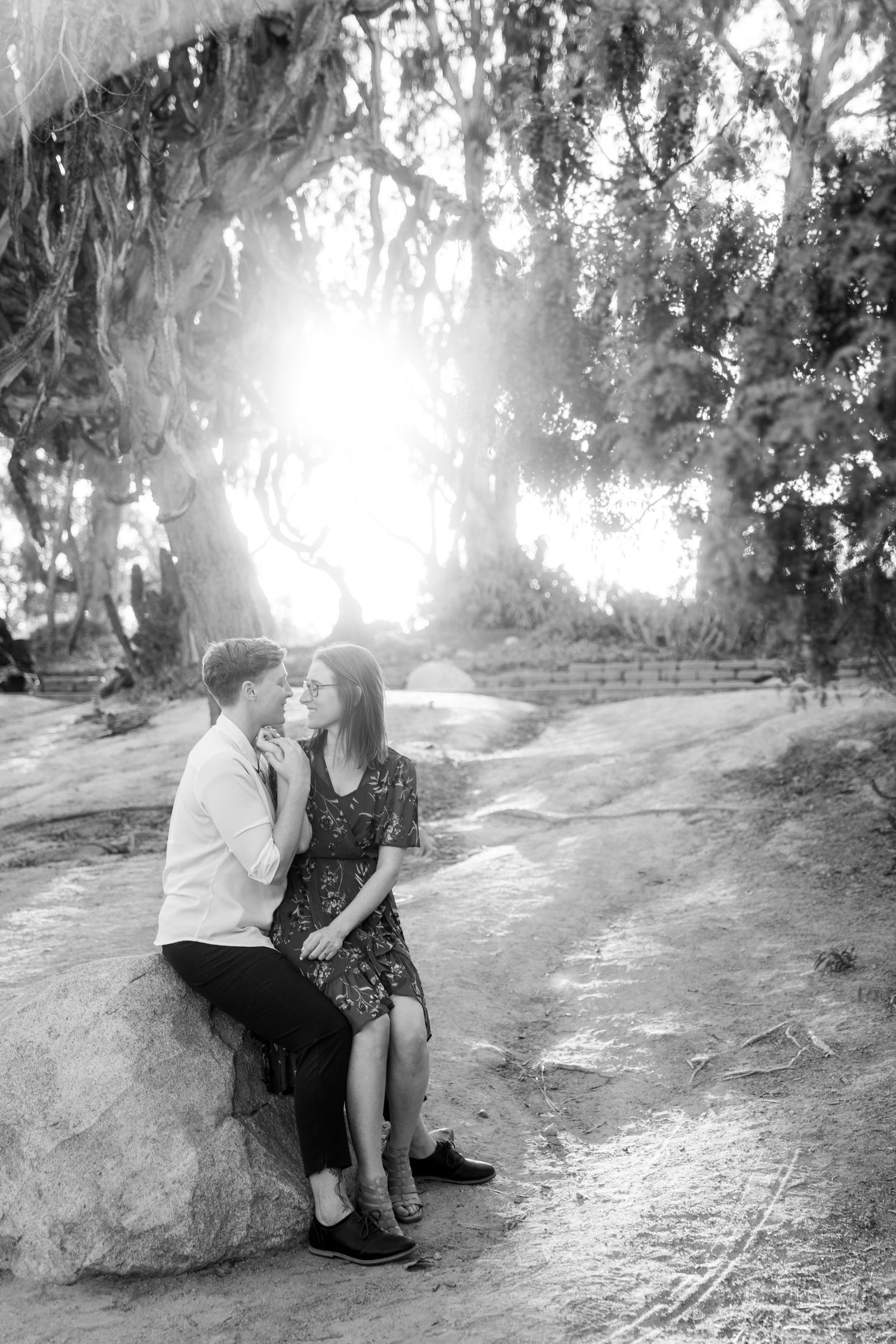 Romantic black and white photo of couple sitting on rock under hanging moss trees.