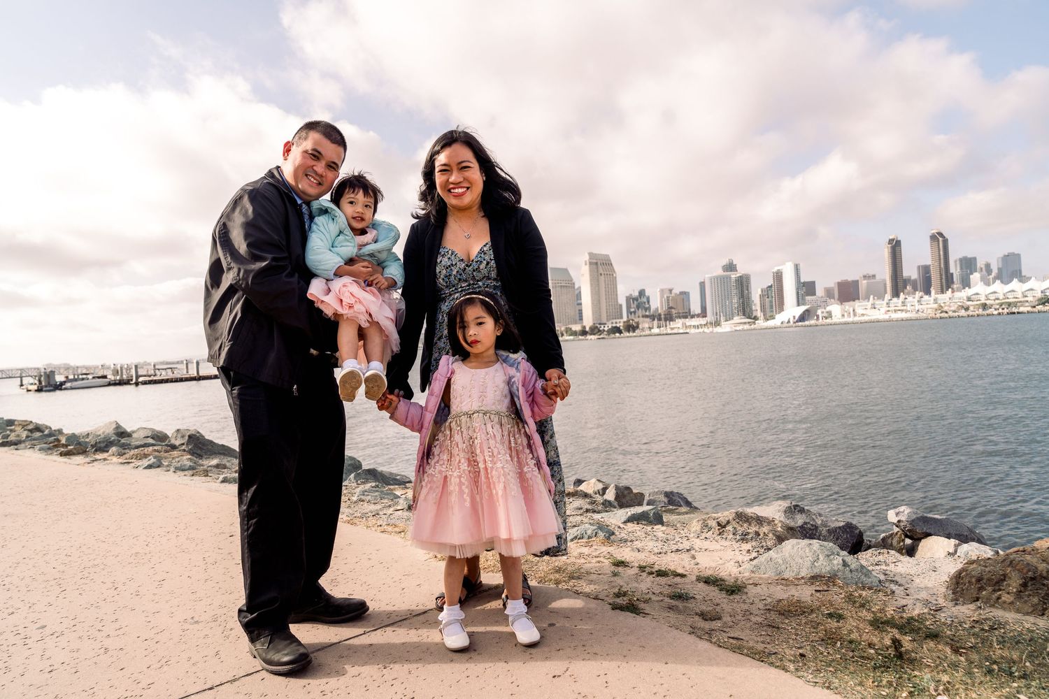 Happy family posing together on waterfront path with city skyline backdrop.
