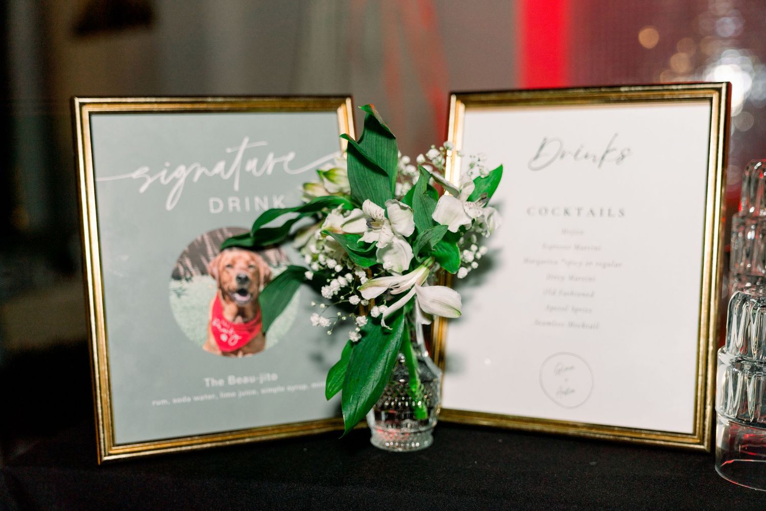 Gold-framed wedding menu displays with small floral arrangement between them.