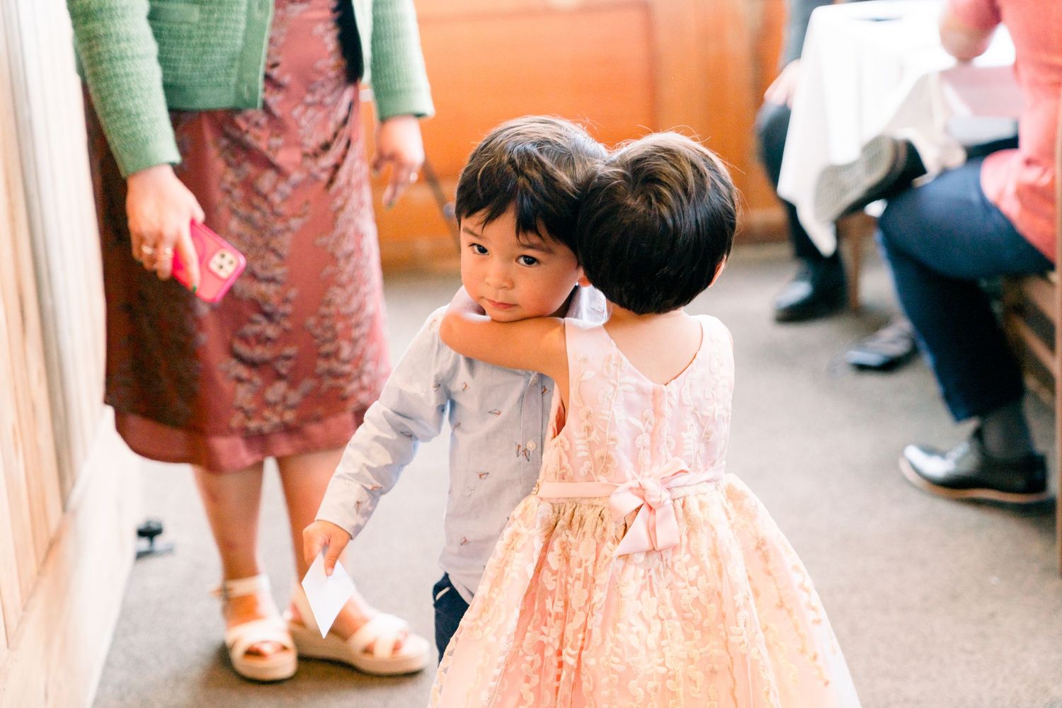 Two young children in formal attire at a wedding event indoors.