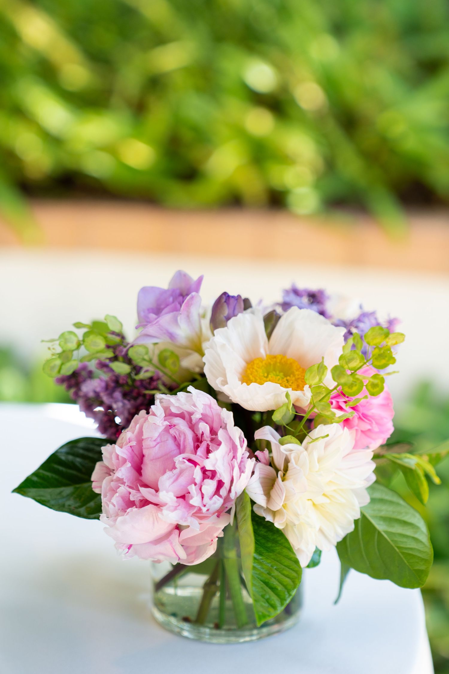 Fresh floral arrangement with pink peonies, purple blooms and white flowers in a glass vase.