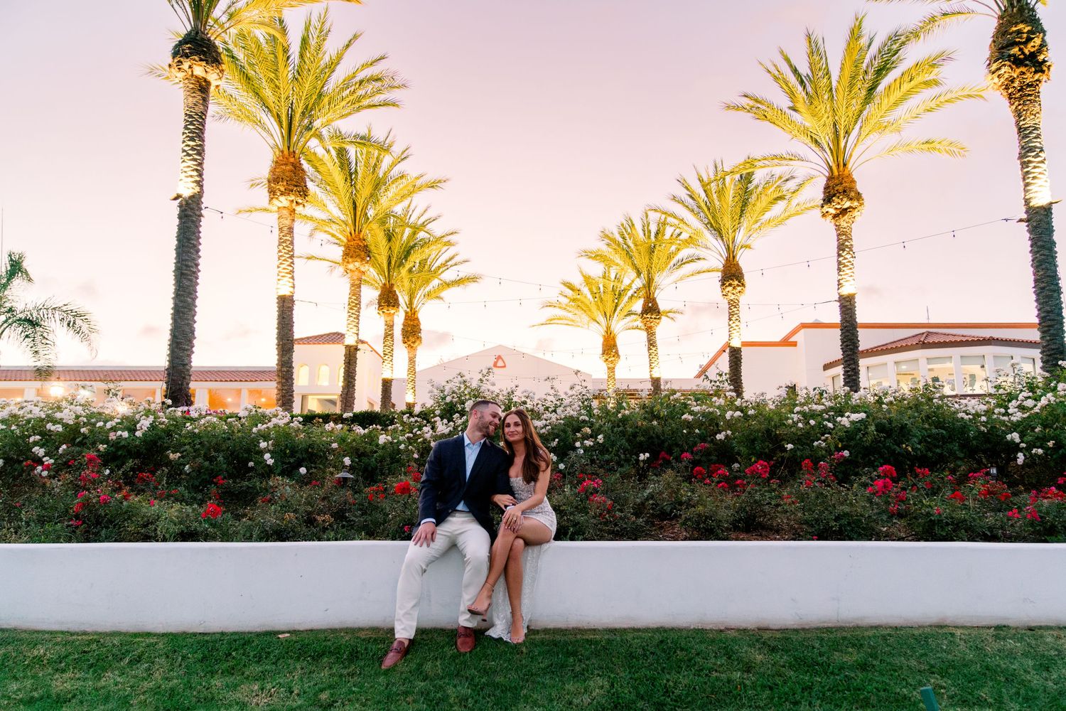 Palm trees frame a romantic scene near a garden wall at sunset.