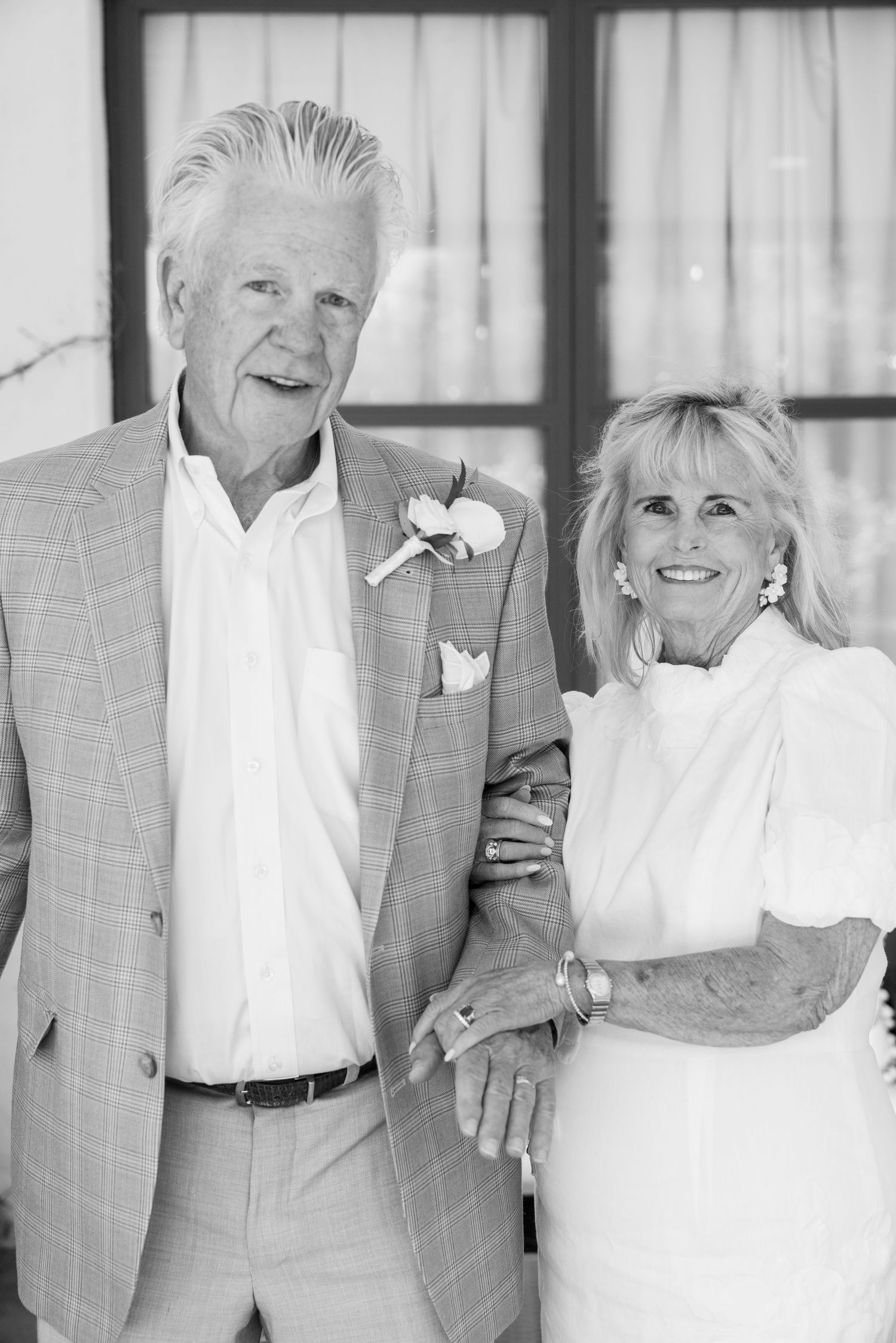 A black and white portrait of an elegant older couple at a formal event, both wearing light colored attire.