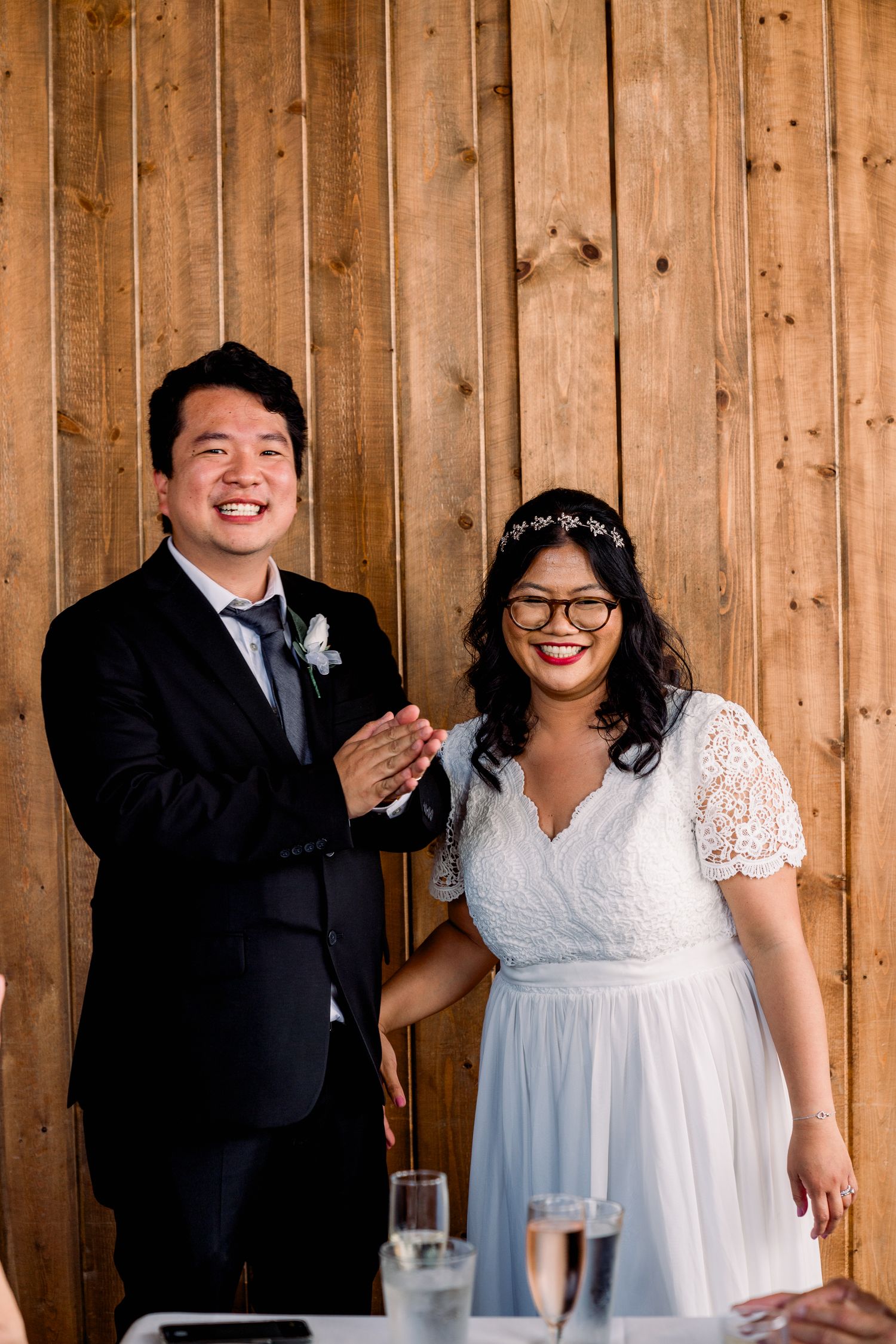 Newlyweds sharing joyful moment against rustic wooden wall backdrop.