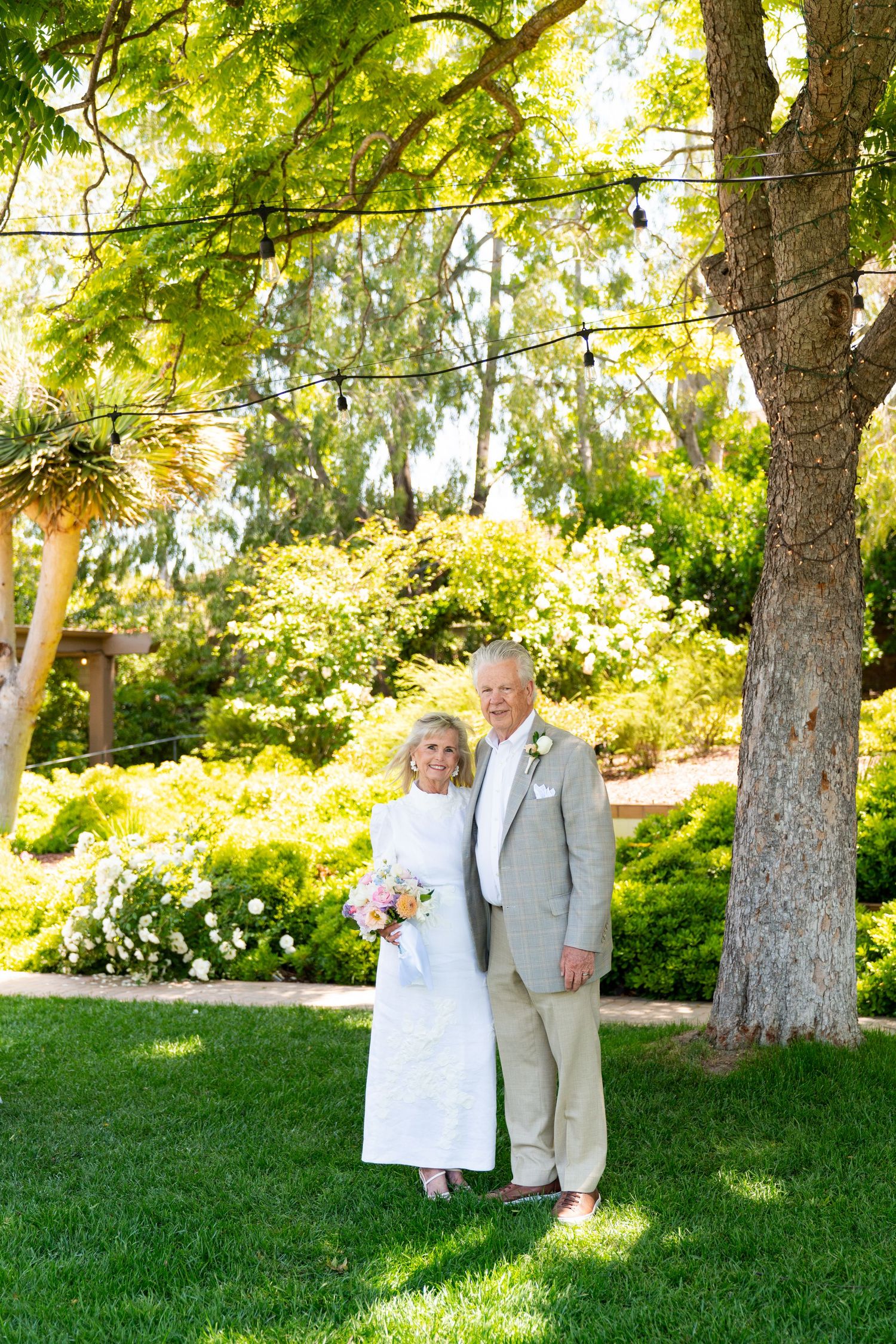 An elegant outdoor wedding portrait framed by lush greenery and trees in a garden setting.