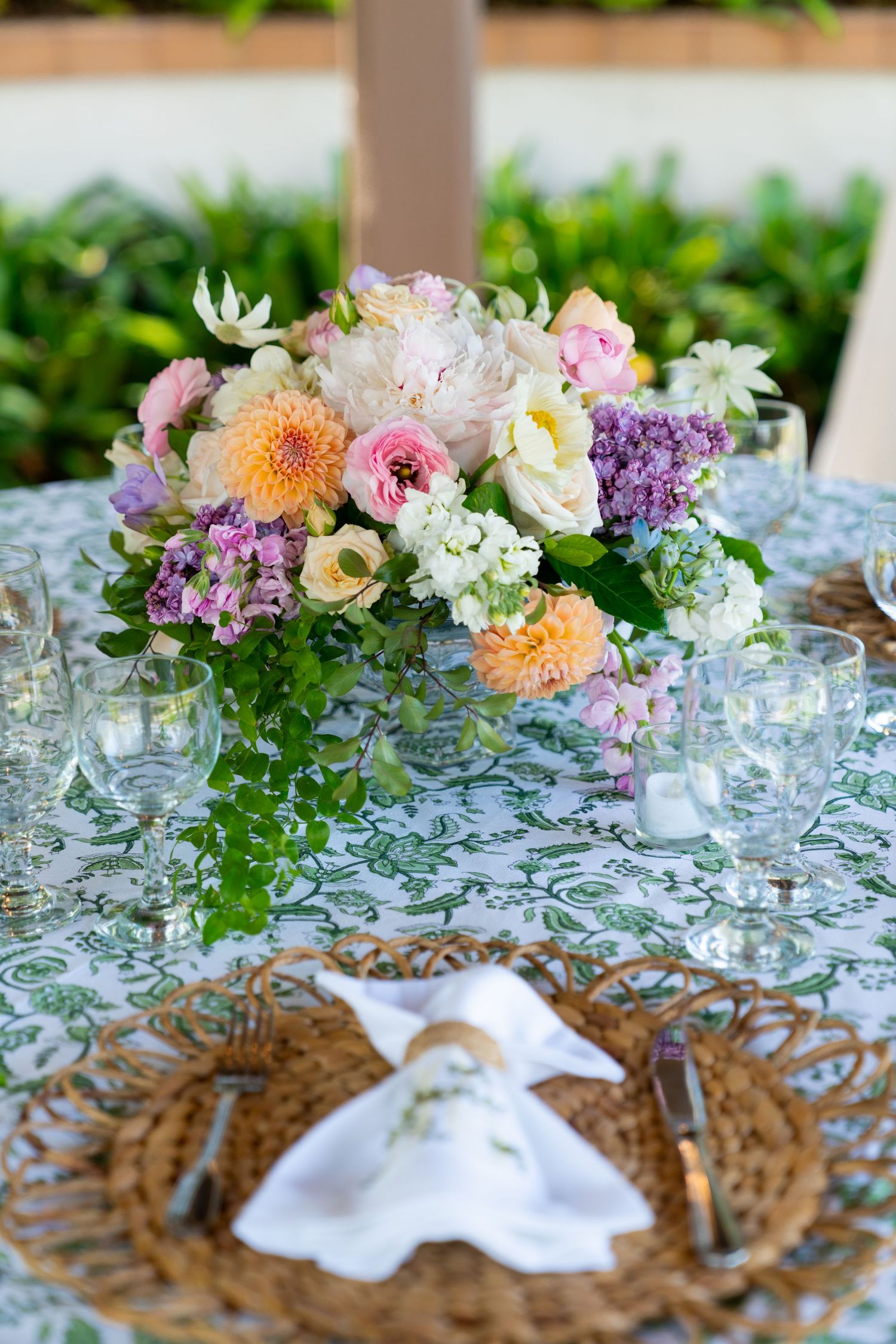 A romantic table setting with a colorful floral centerpiece and woven charger plates on a patterned tablecloth.