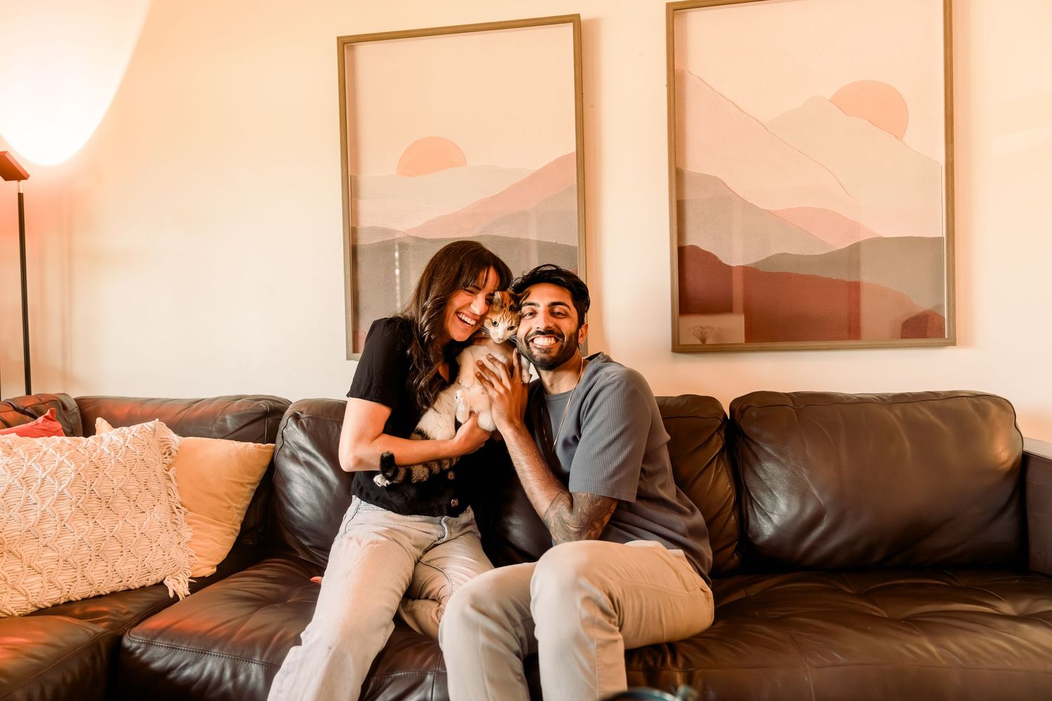 Couple laughing together on a leather couch with decorative wall art and throw pillows.