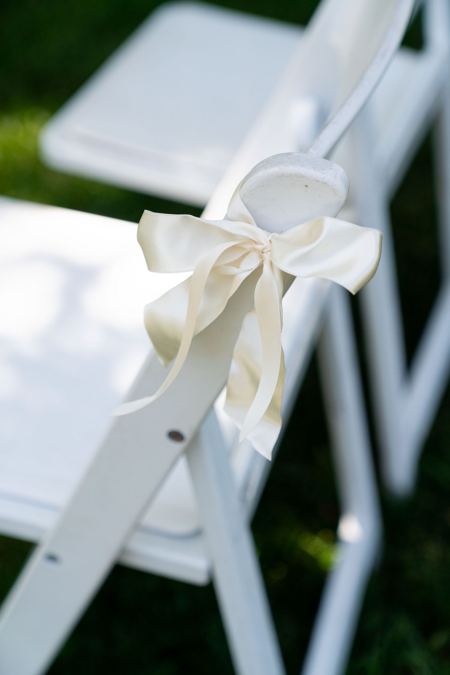White satin bow decorating a folding chair, perfect for wedding ceremony seating.