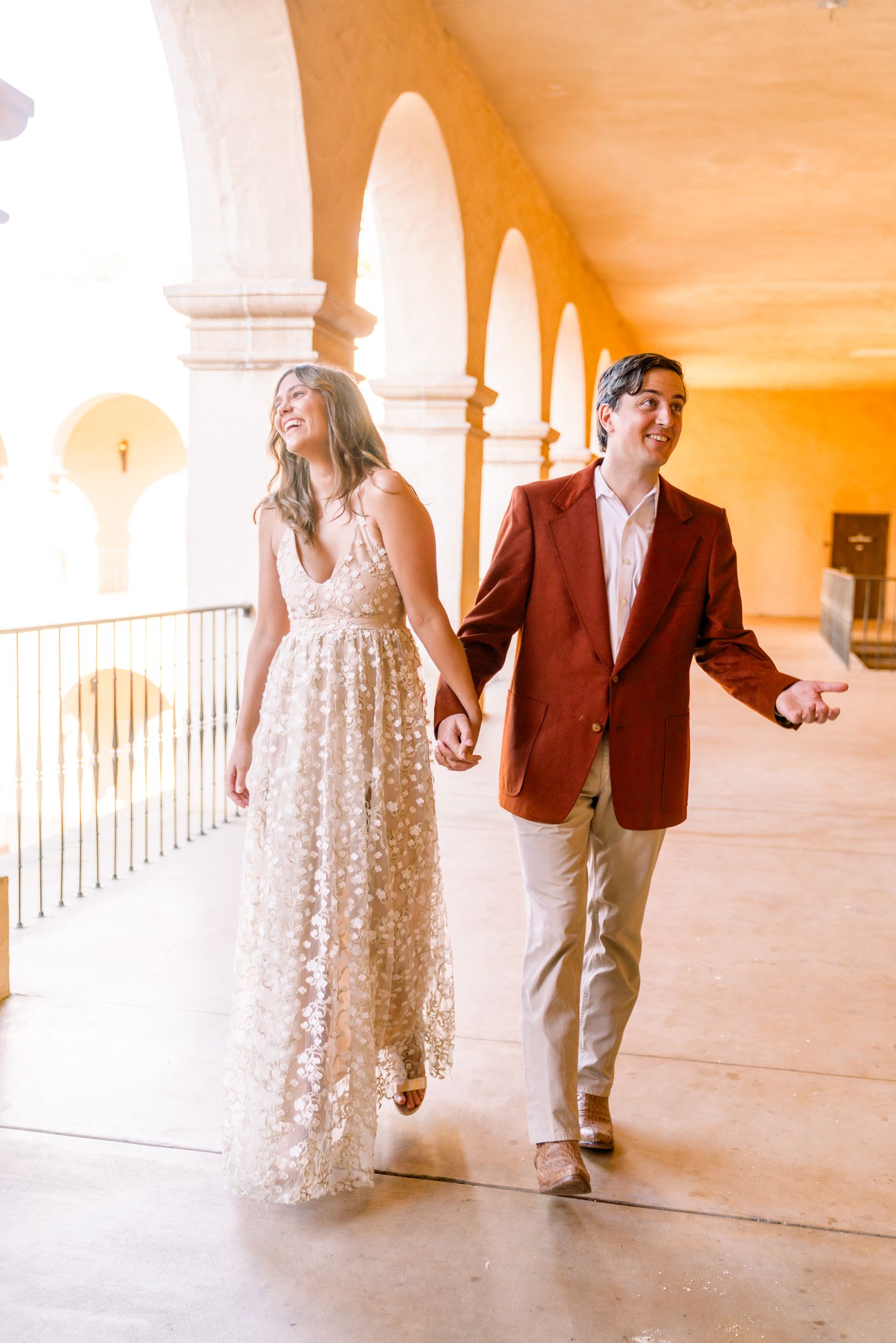 Couple walking through arched corridor in formal attire during golden hour.