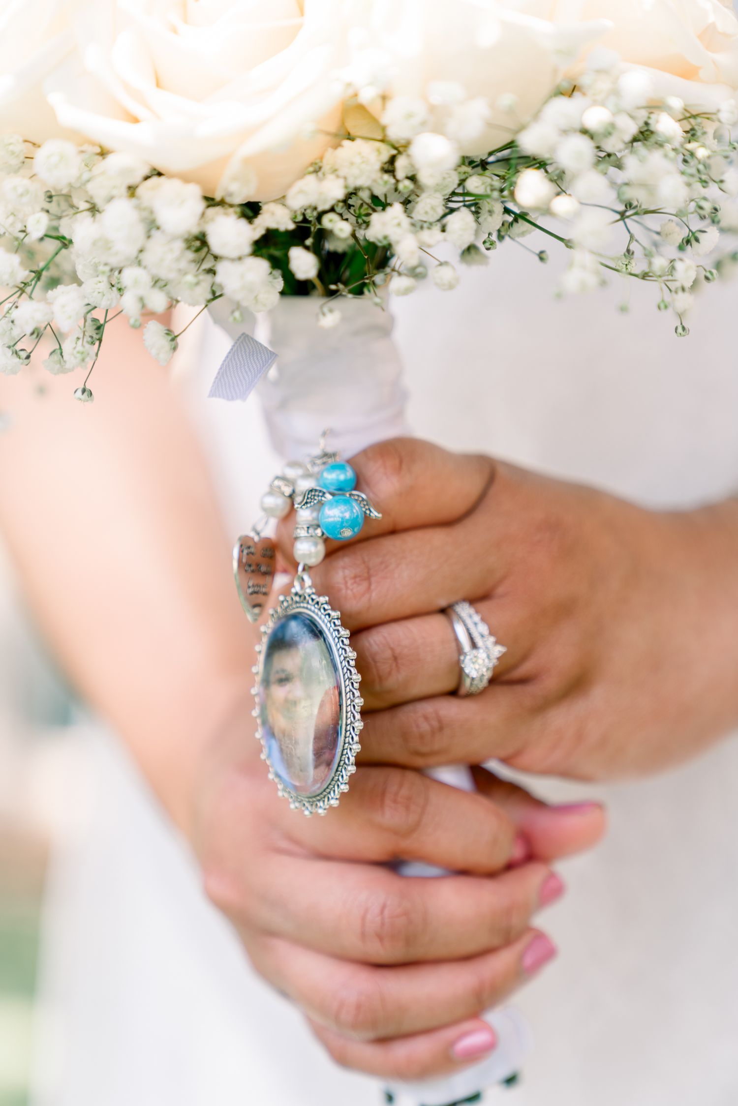 Close up of bridal bouquet with white flowers and a sentimental photo locket charm attachment.