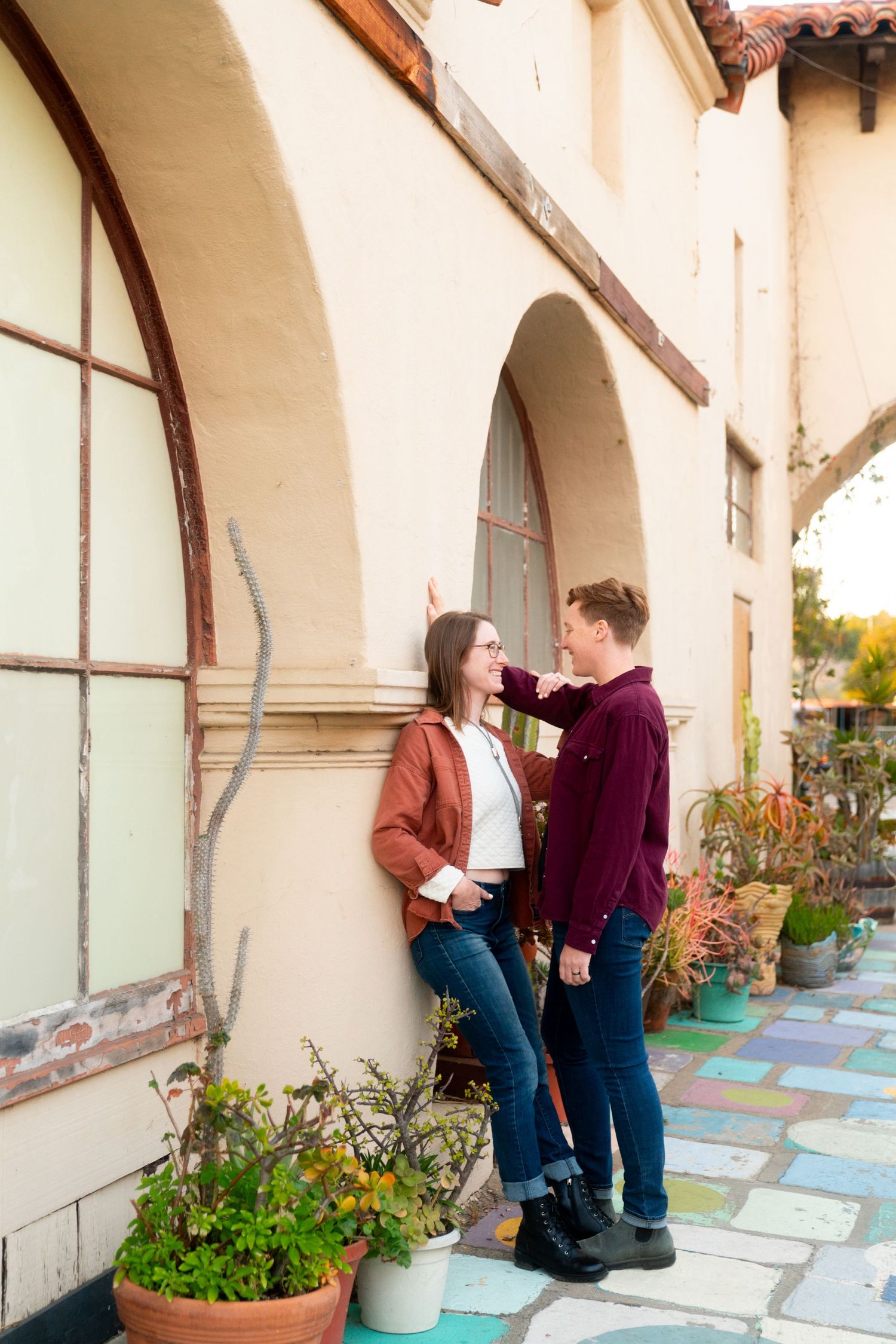 Two people share a tender moment against cream-colored Spanish colonial architecture.