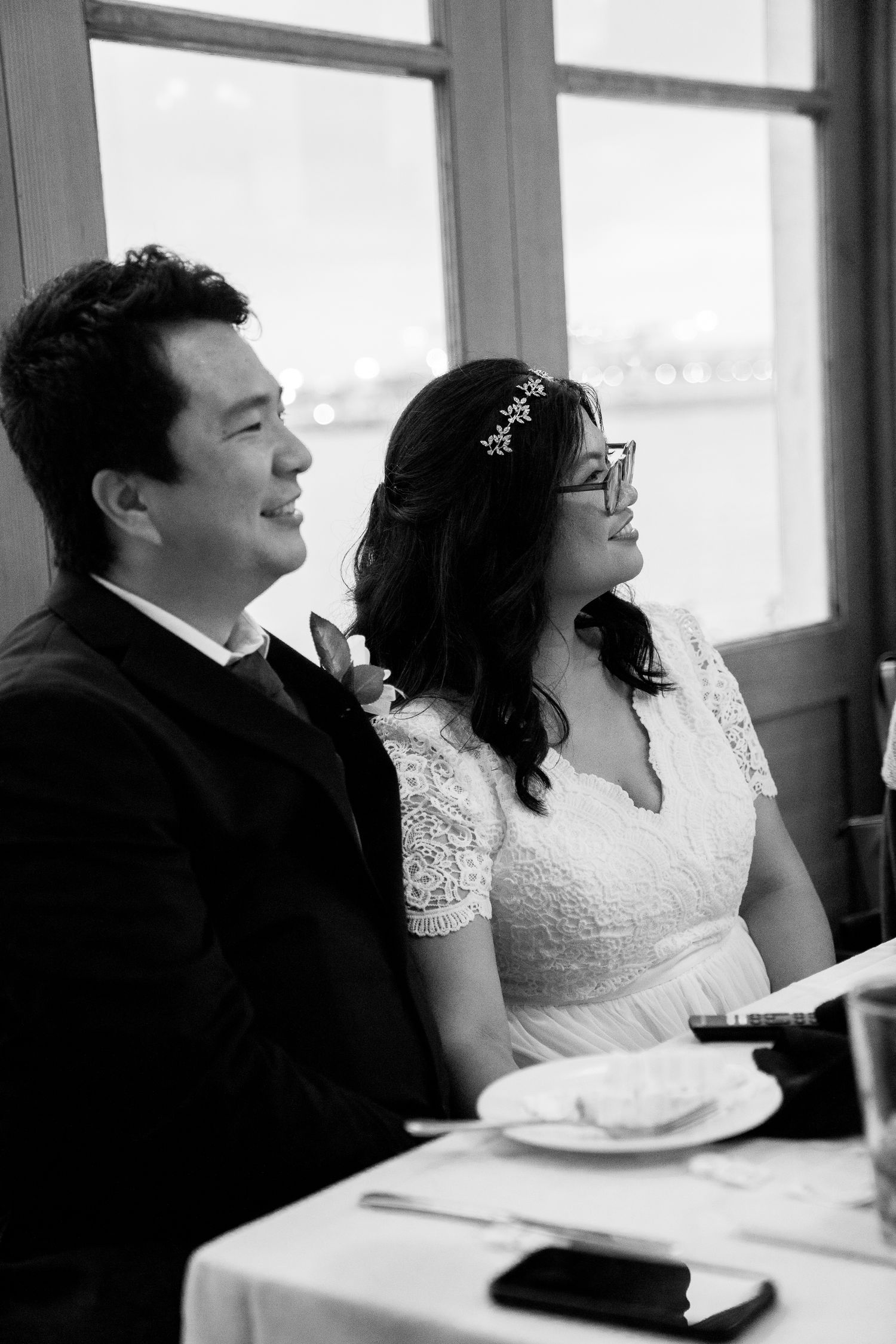 A black and white candid moment of a couple seated at their wedding reception.