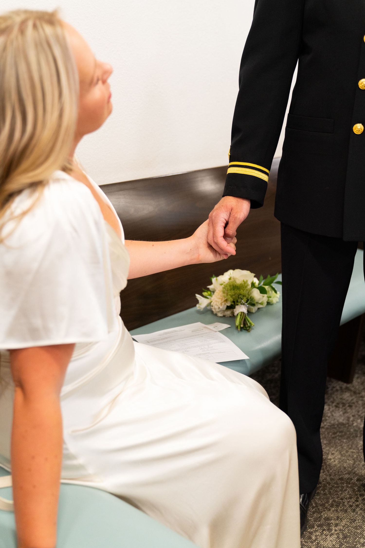 A bride in a white dress holds hands with someone wearing a formal military uniform at a wedding ceremony.