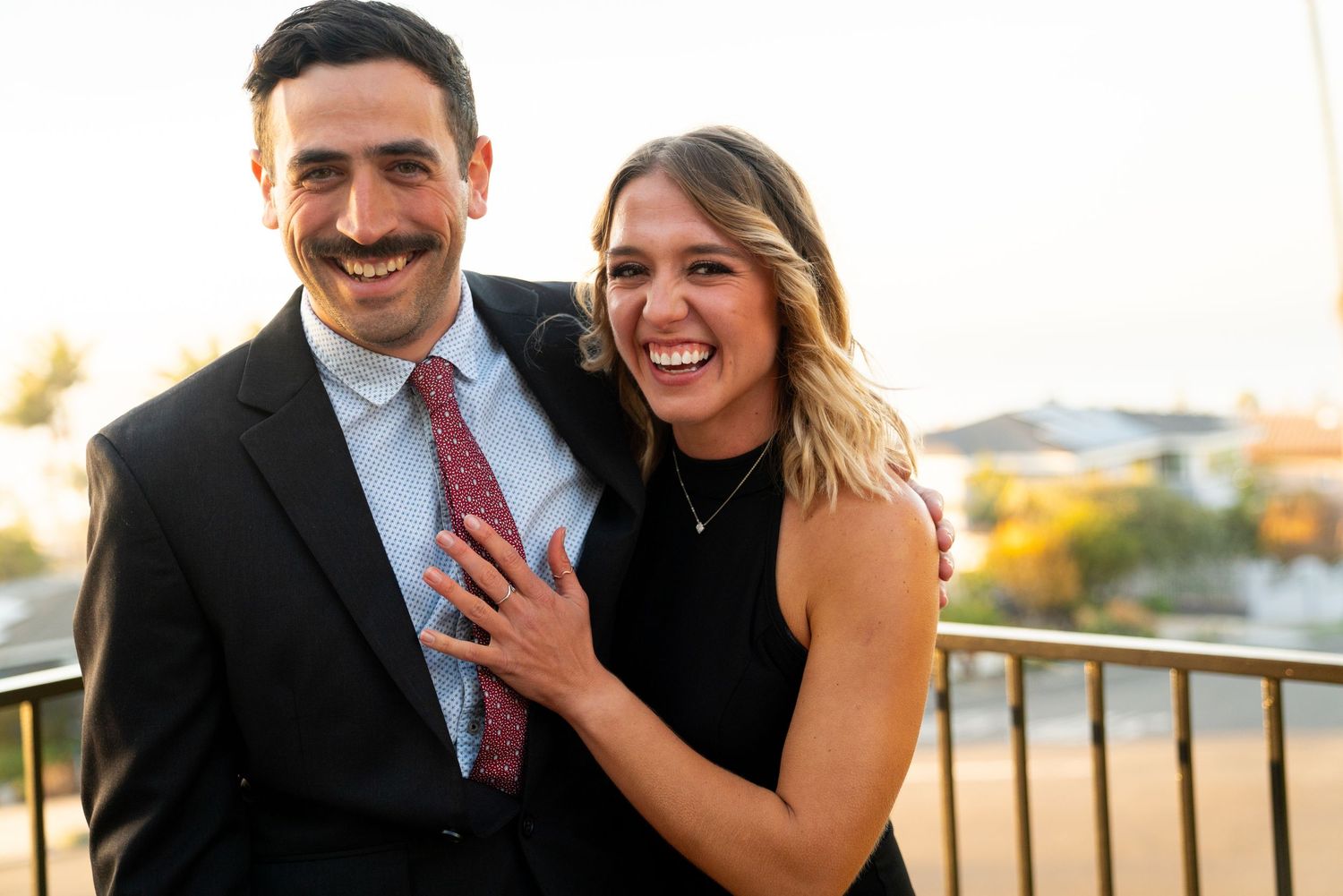Newly engaged couple laughing together during sunset on a balcony.