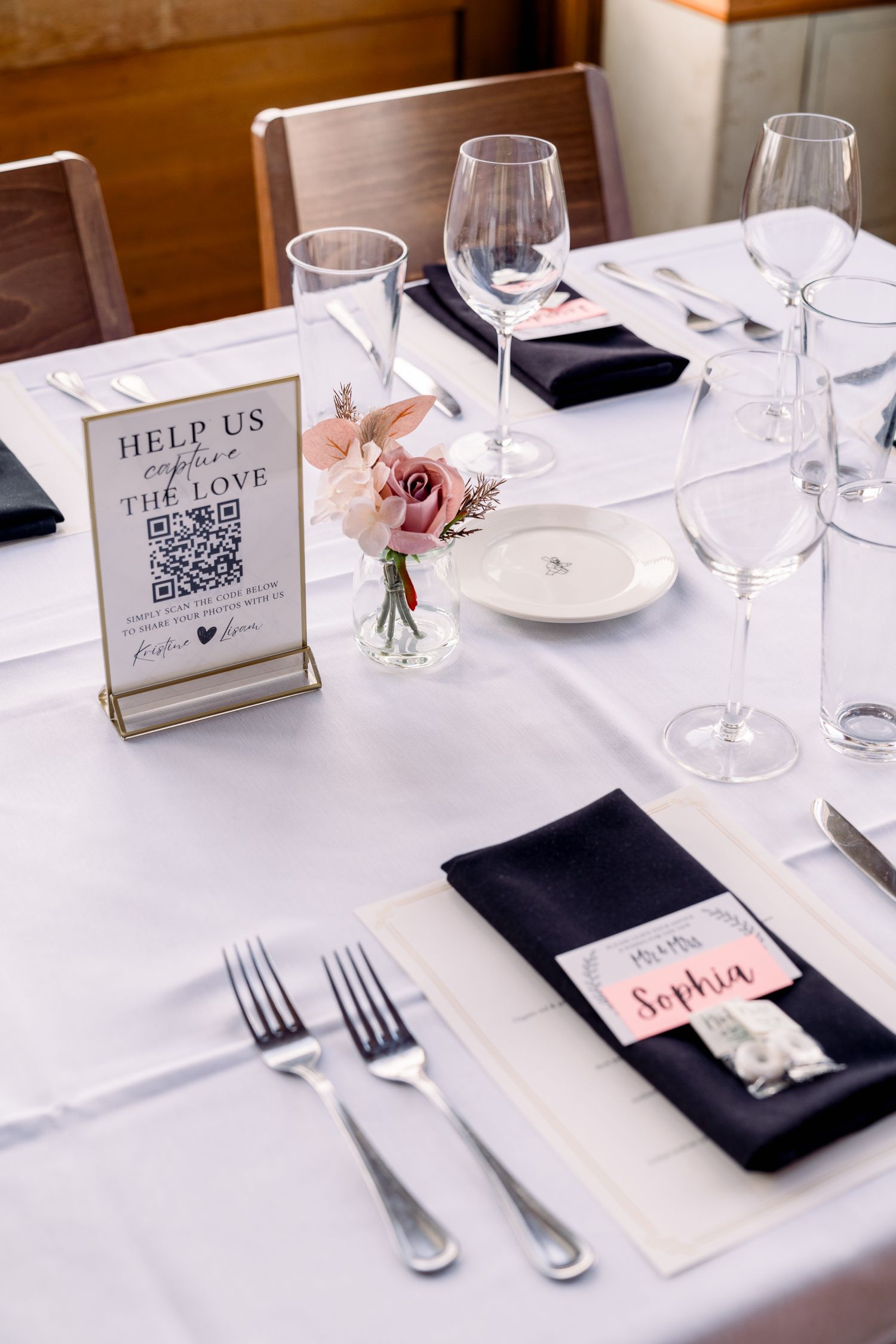 Elegant wedding table setting with QR code sign, wine glasses, and pink flower centerpiece.