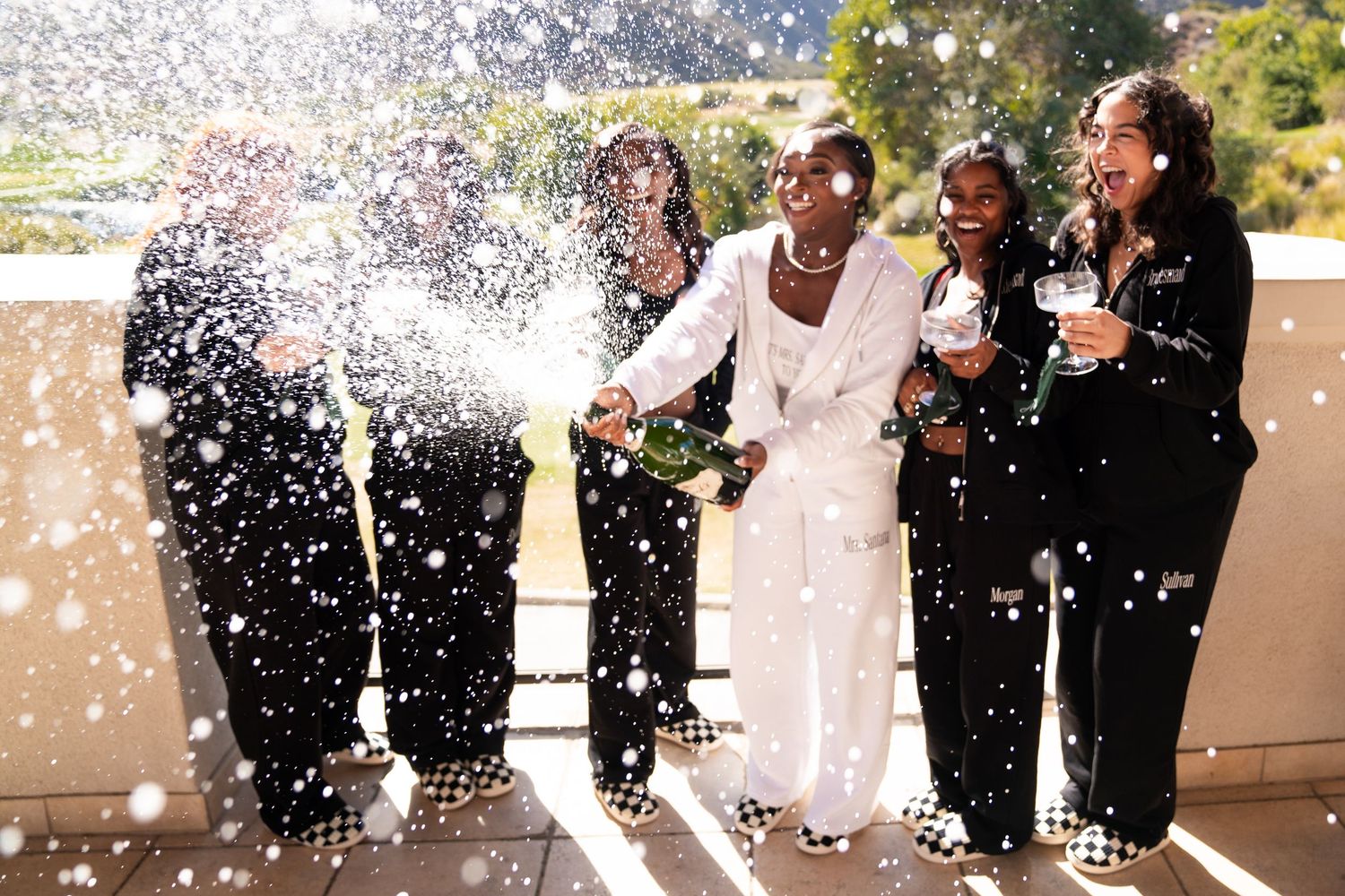 Group of friends laughing and celebrating with champagne spray on an outdoor balcony.