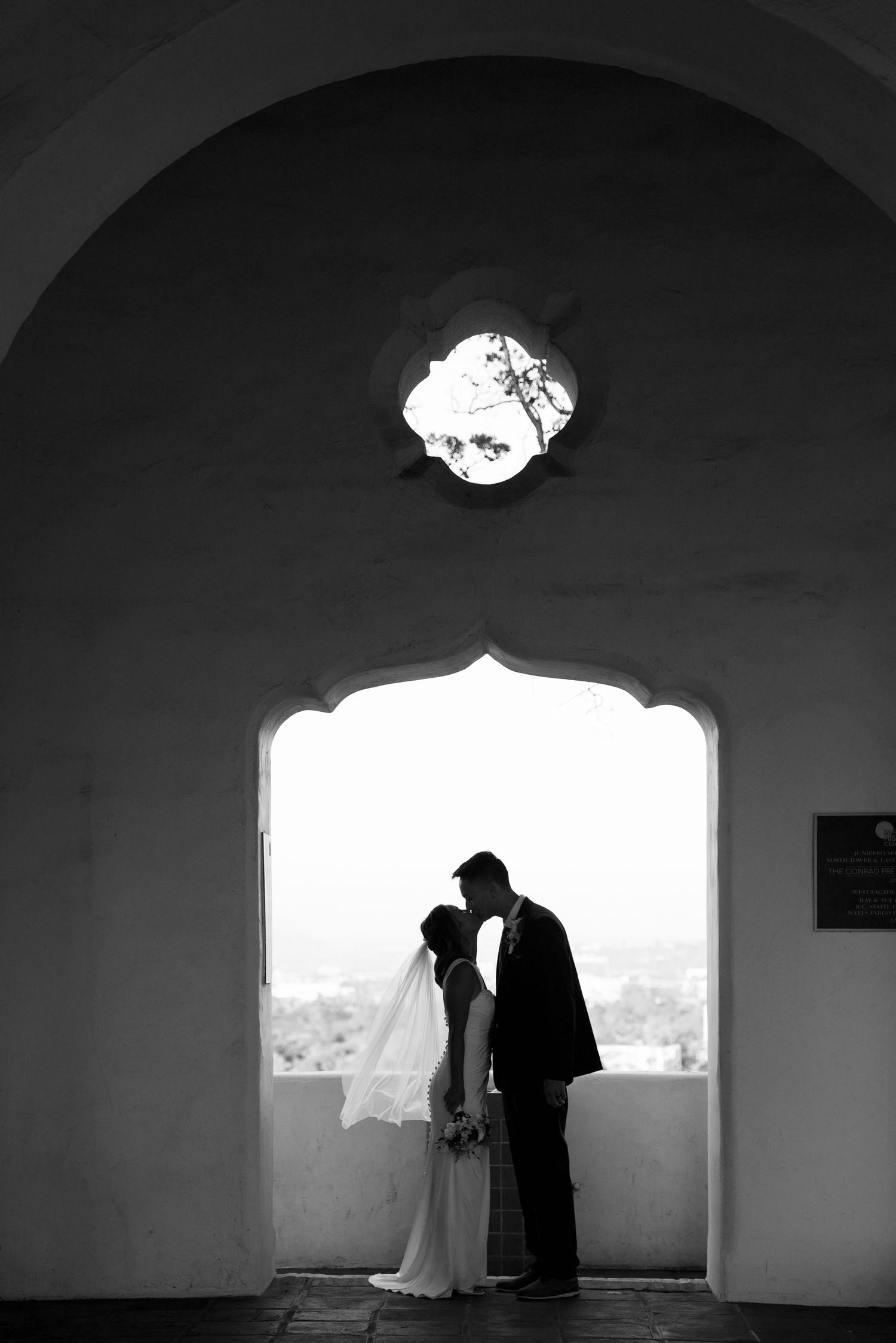 A romantic silhouette of a couple in an arched doorway with a circular window above creating a dramatic black and white scene.