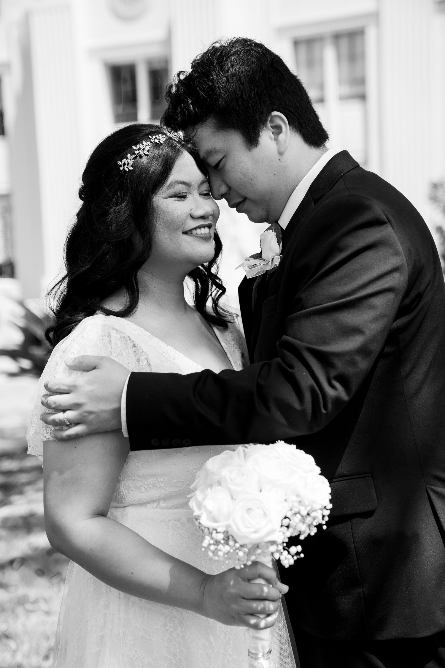 Black and white portrait of a romantic wedding couple embracing while the bride holds a white bouquet.
