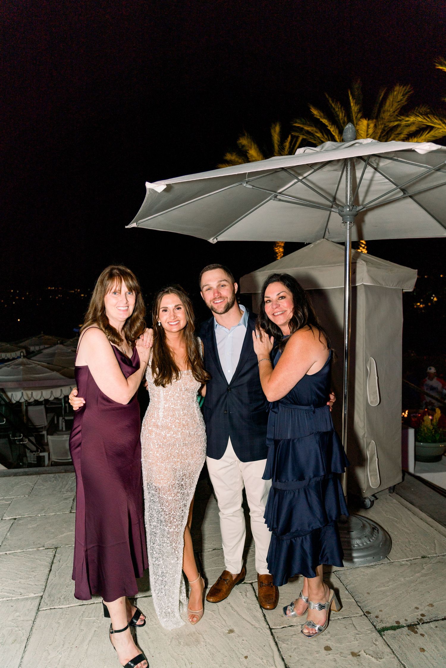 Group poses under white umbrella during evening outdoor celebration.