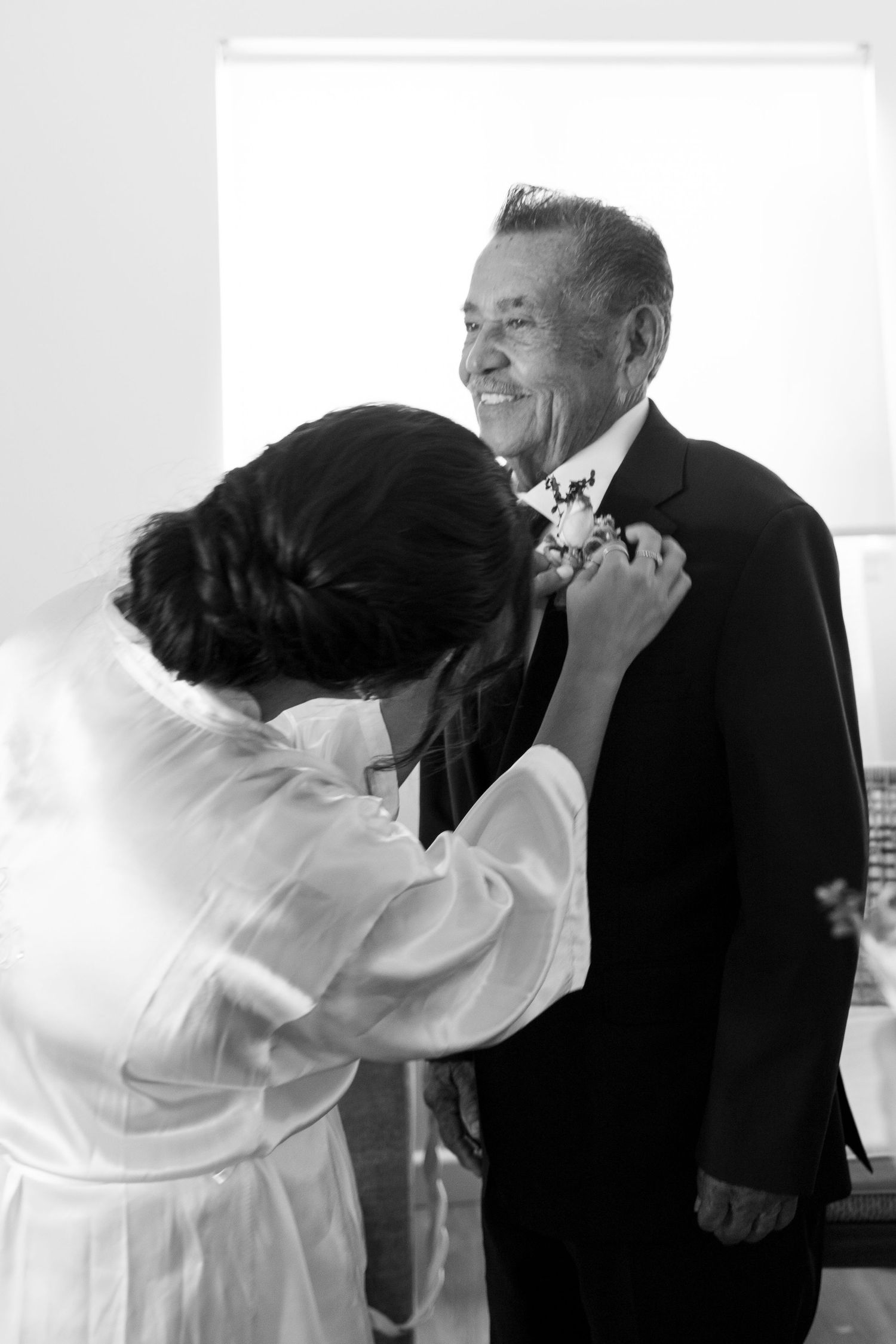 A tender moment captured in black and white as someone helps adjust a formal tie or boutonniere.