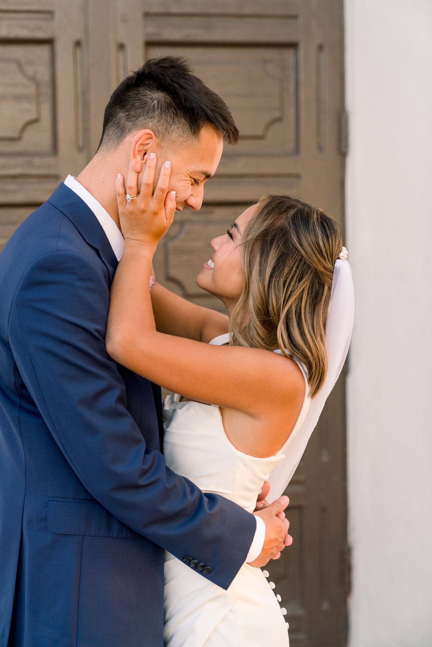 A tender moment between newlyweds sharing an intimate embrace against wooden doors.
