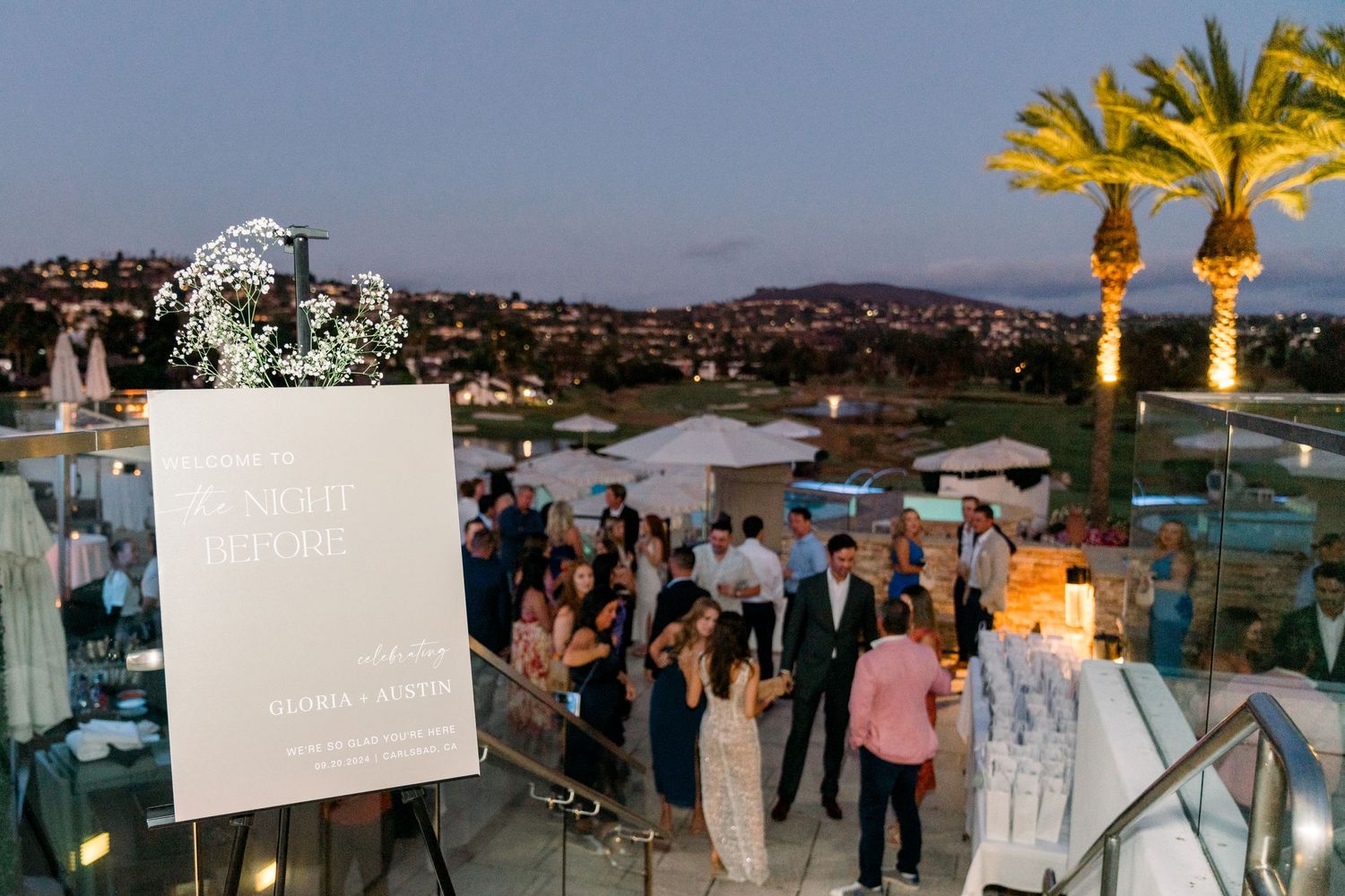 An evening outdoor event with illuminated palm trees and guests mingling.