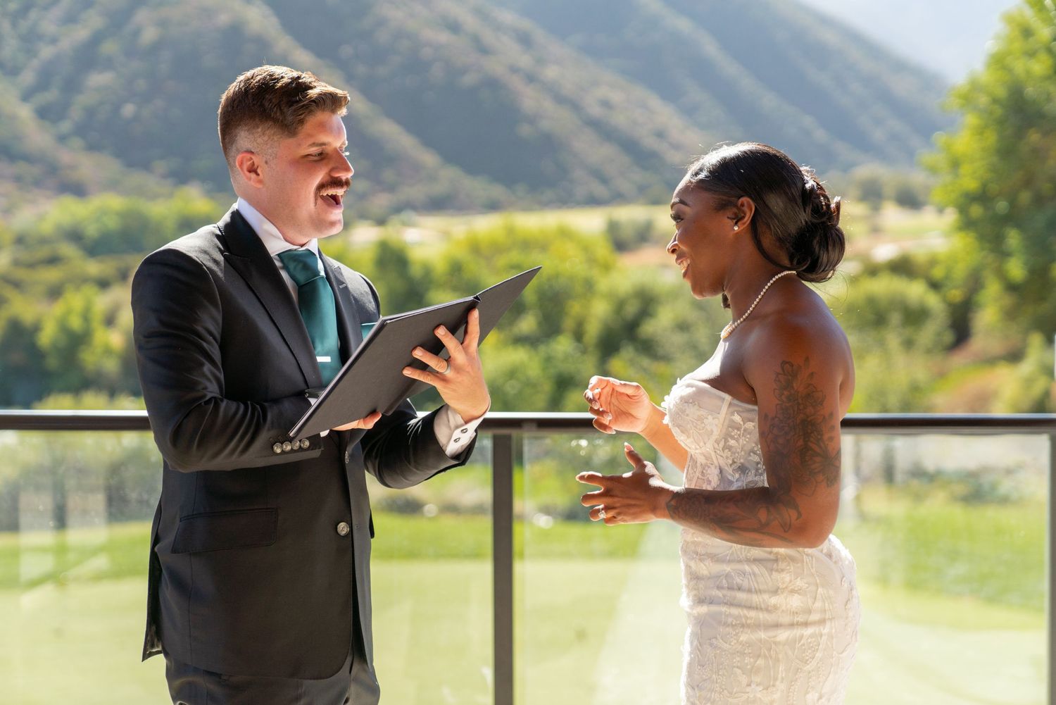 Couple sharing joyful moment during outdoor wedding ceremony against mountain landscape.