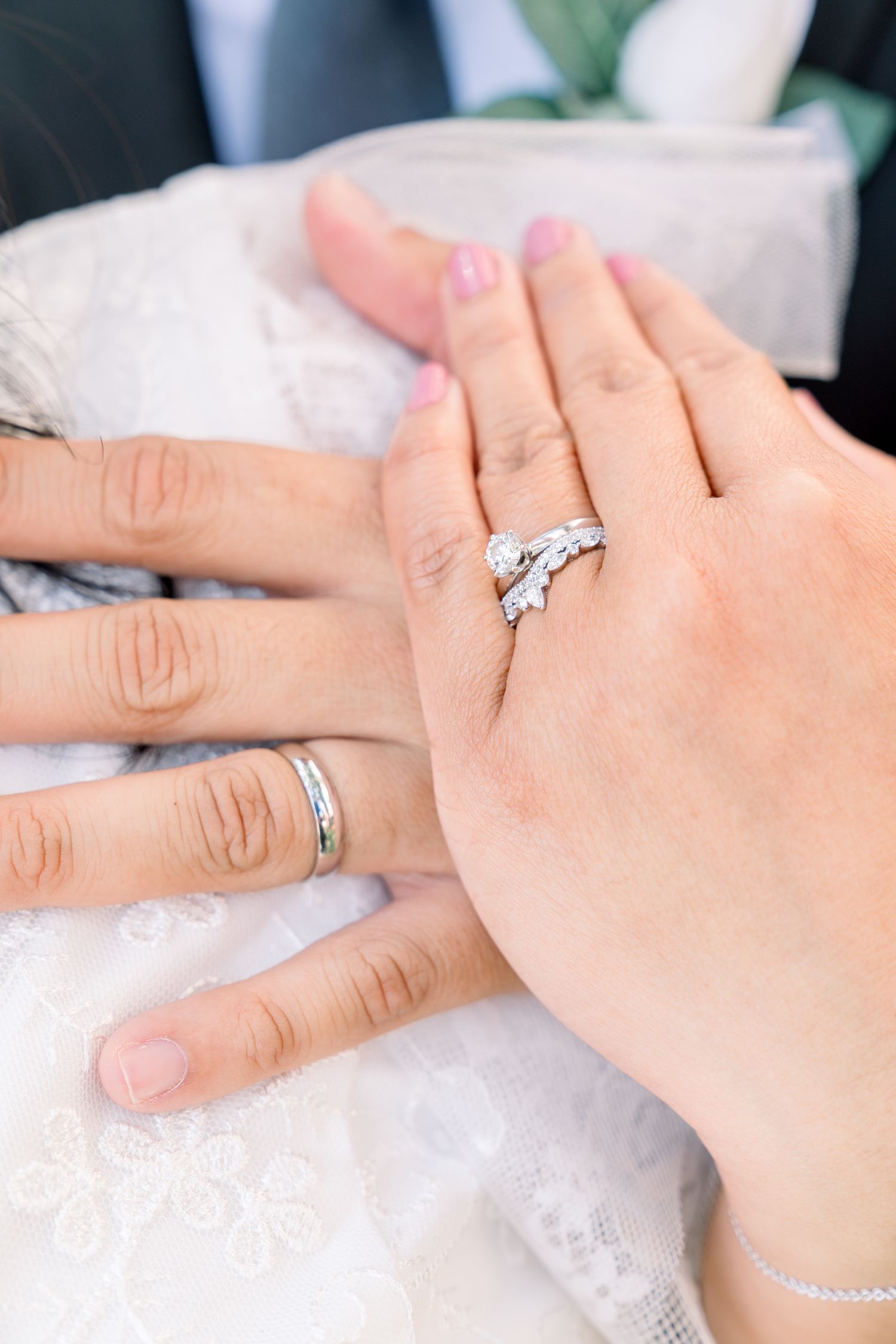 Close-up of hands showing elegant diamond wedding rings on white fabric.