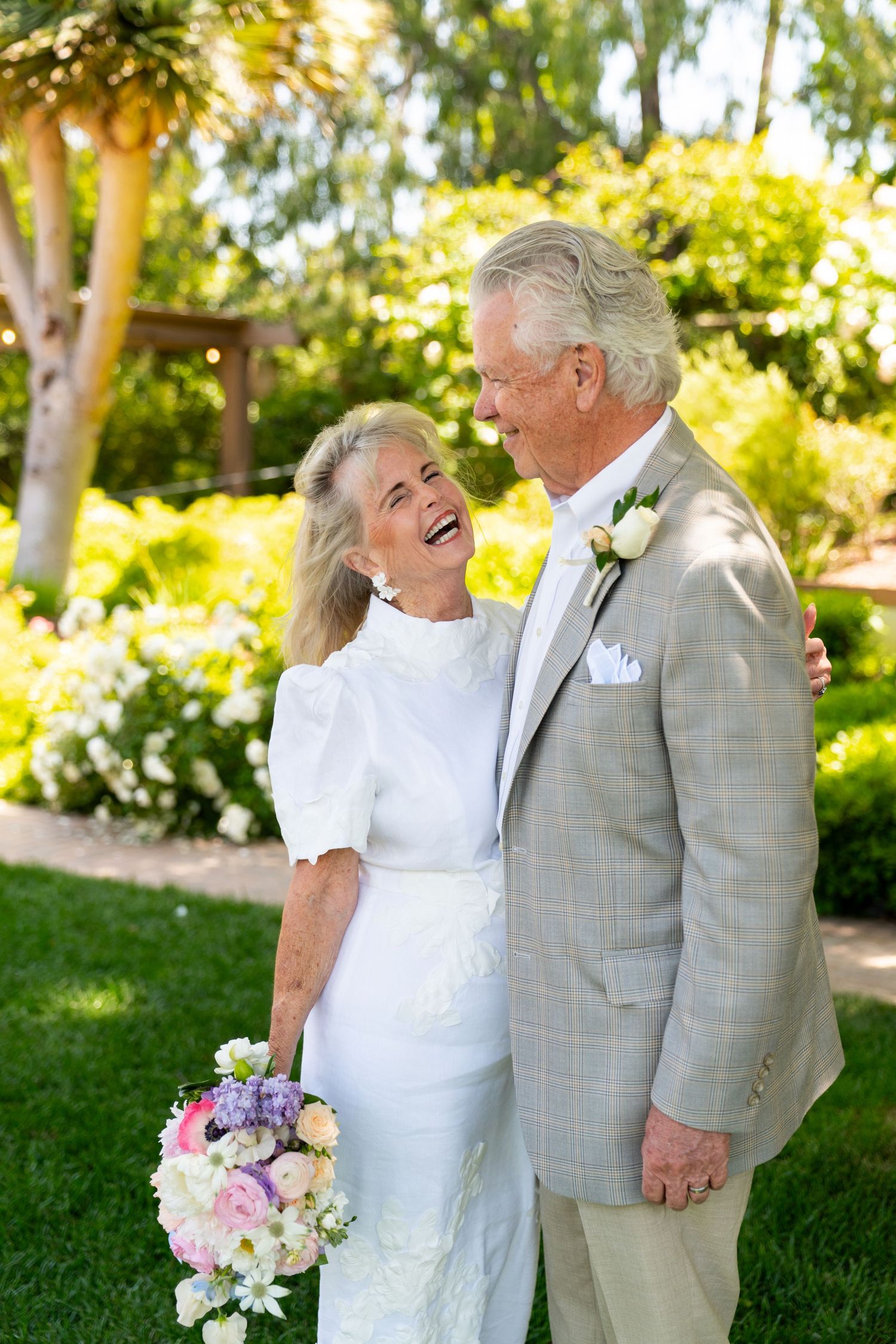 A joyful couple sharing a laugh together in a sunlit garden setting.