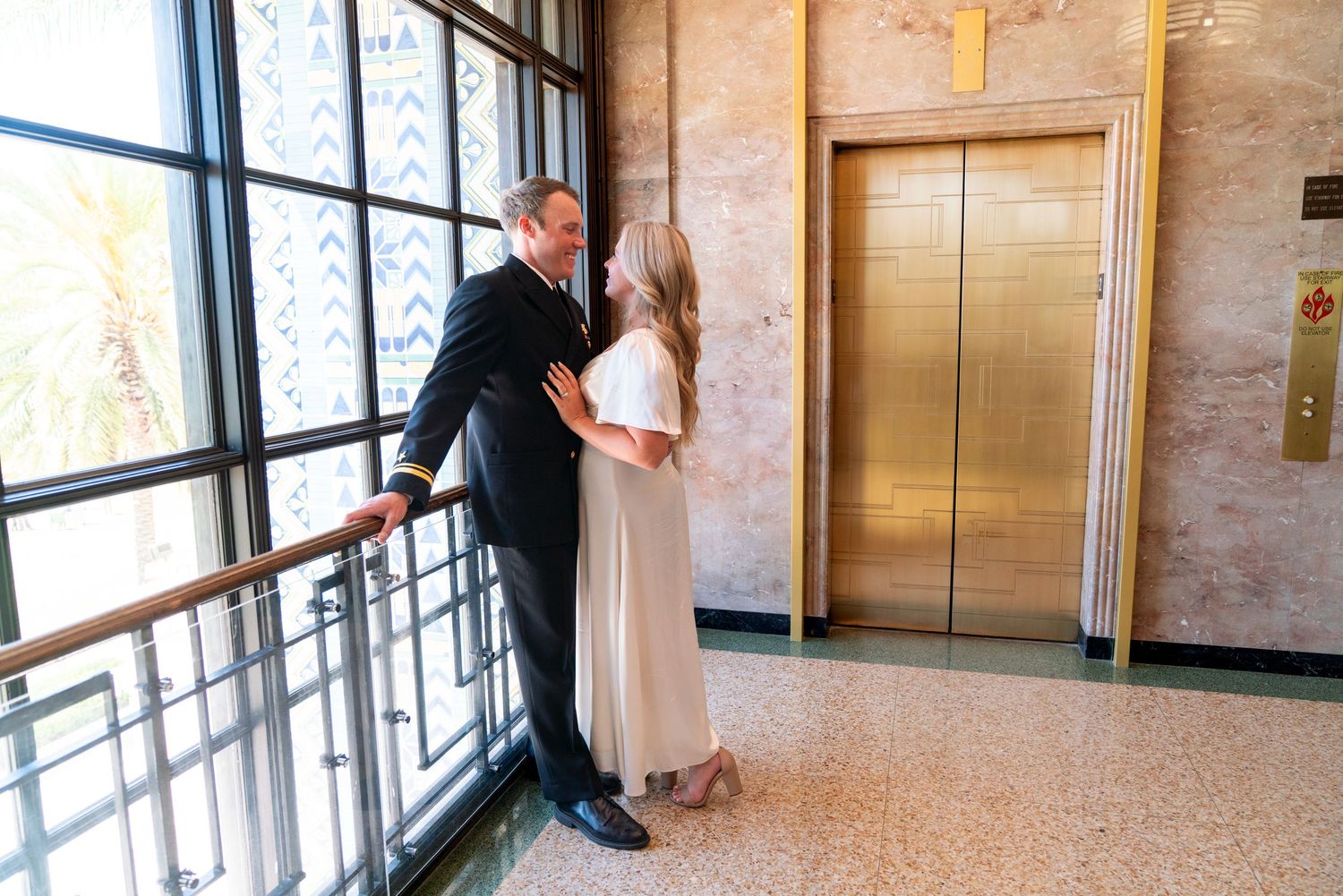 A newly married couple embraces in a softly lit church hallway with large windows casting natural light.
