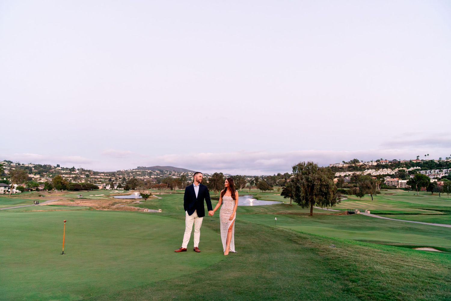 Two people walking together on a lush green golf course with rolling hills in the background.
