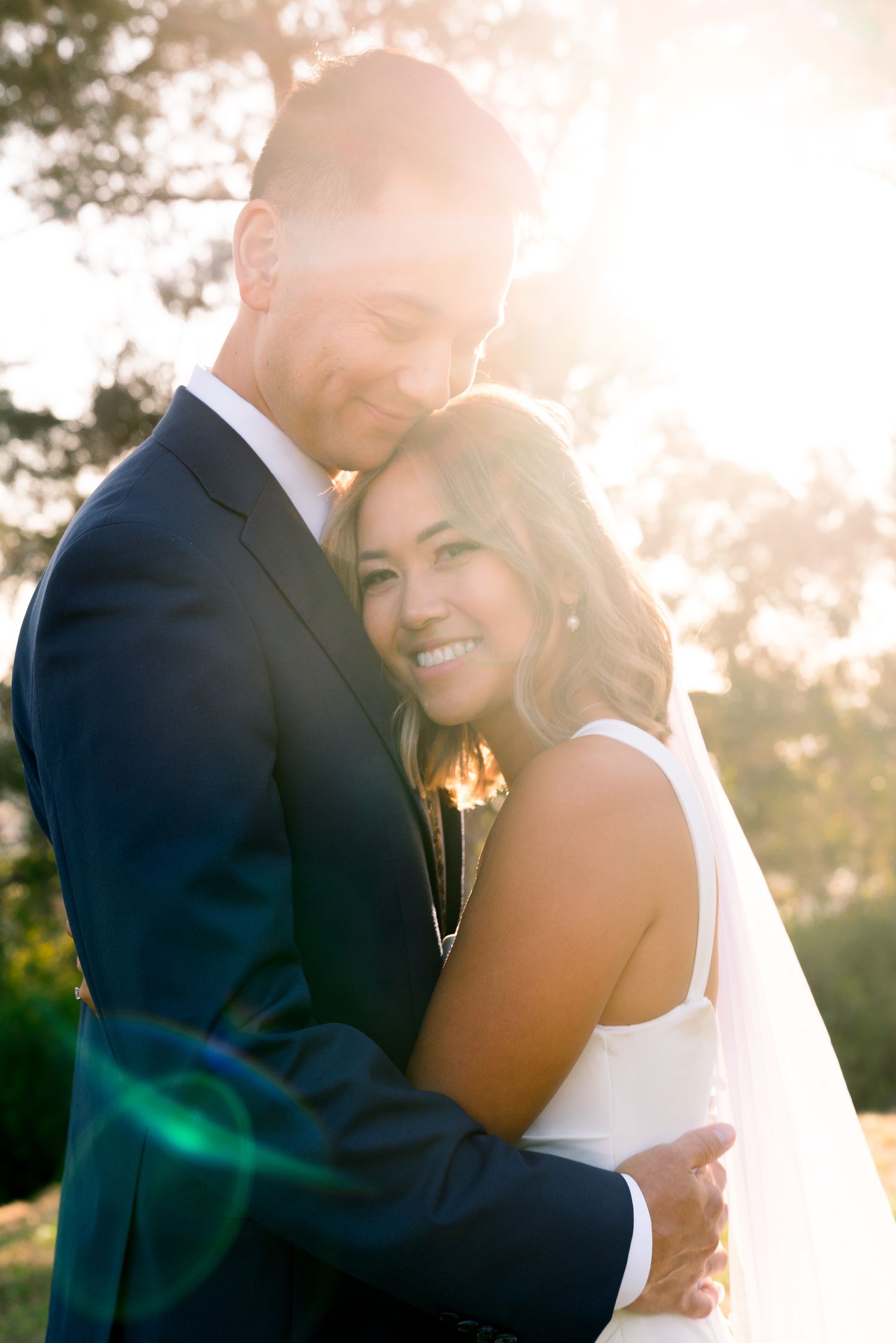 A joyful wedding couple embraces in golden sunlight during an outdoor photoshoot.